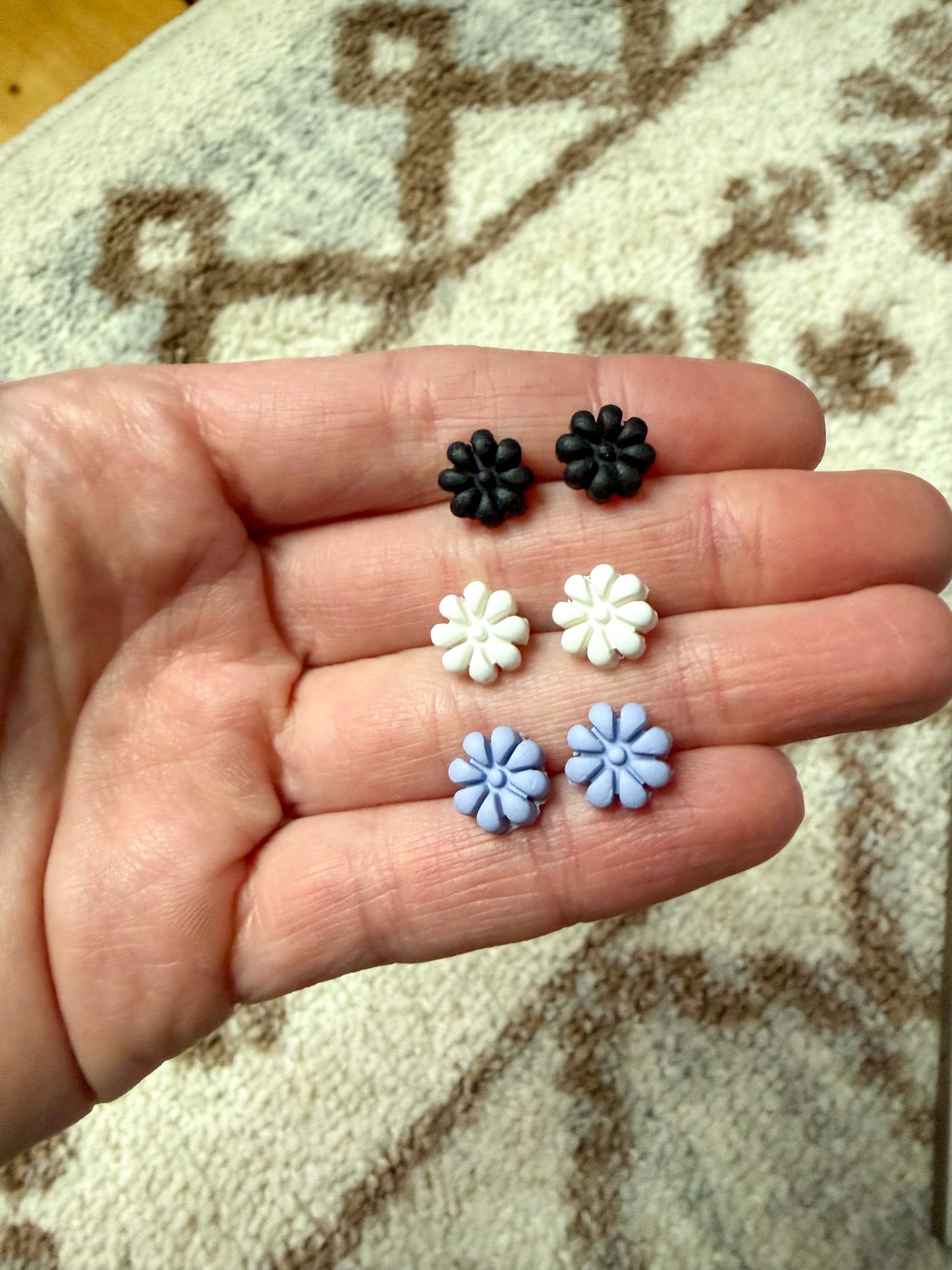 Hand holding three pairs of small flower-shaped earrings against a textured surface.