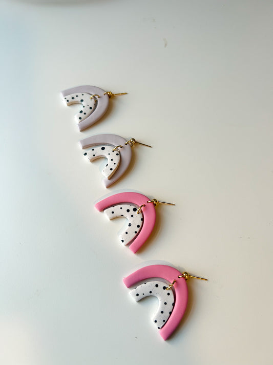 Double rainbow shaped dangles. The tops are either light pink or purple and the bottoms are polkadot. Both pairs are laying on a flat surface. 