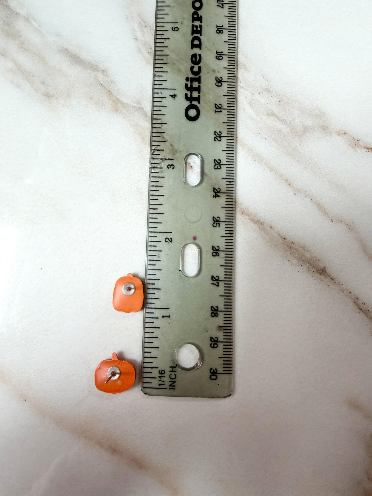 Small orange earrings next to a ruler for scale. About half an inch long. 