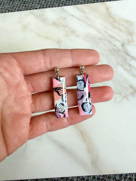 Butterfly pattern on colorful earrings, held in a hand.