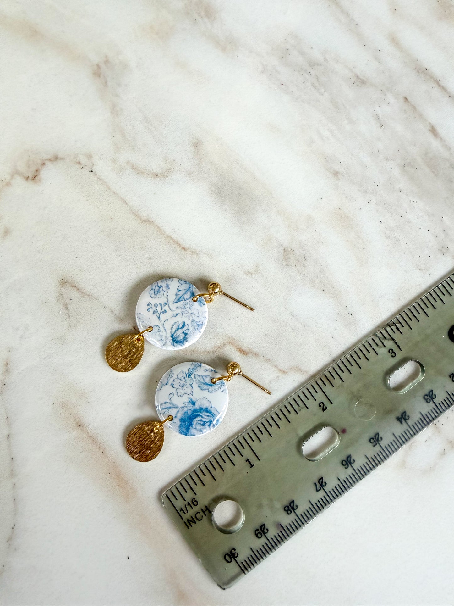 Pair of earrings with floral design next to a ruler on a marble surface