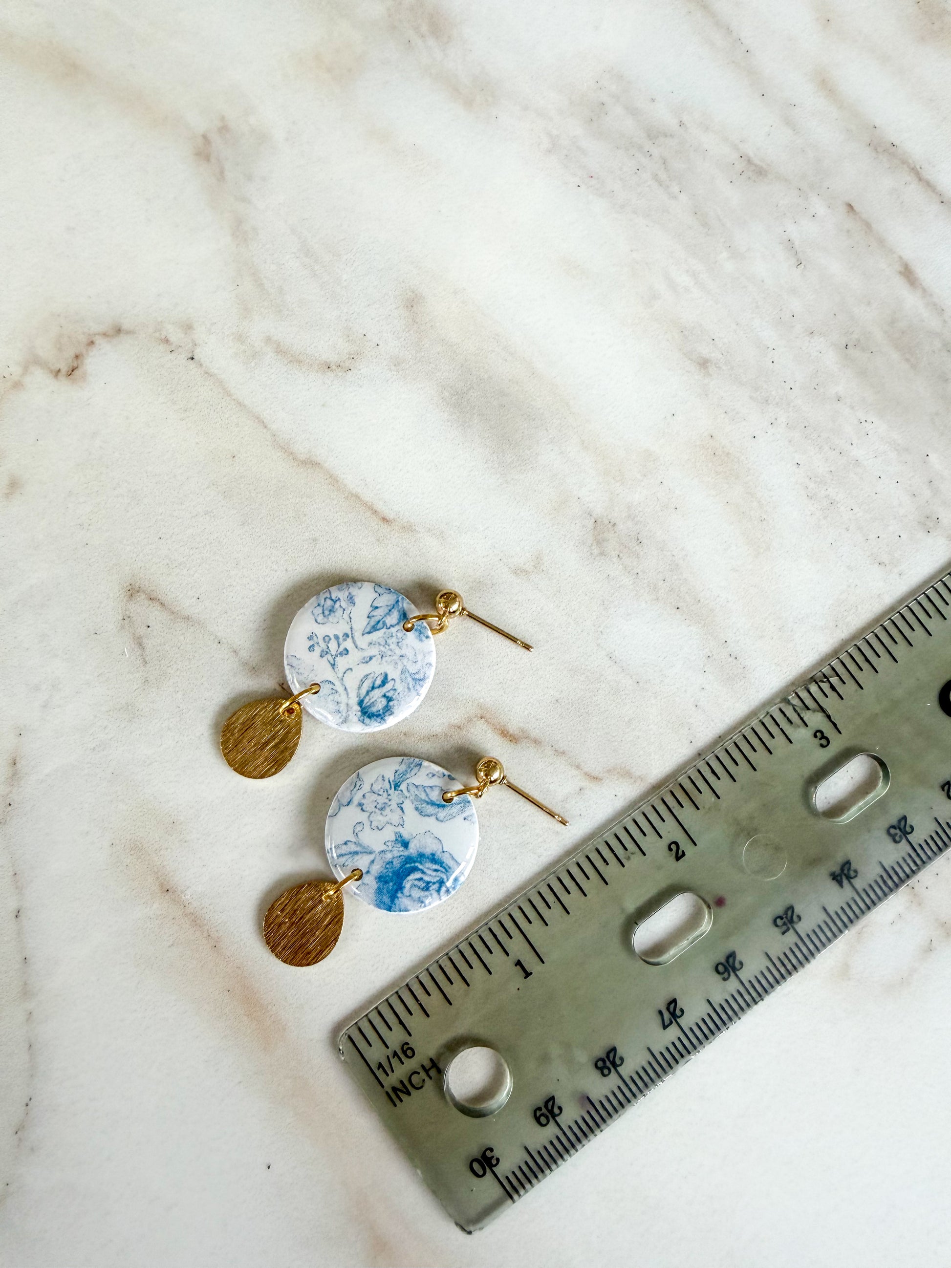 Pair of earrings with floral design next to a ruler on a marble surface