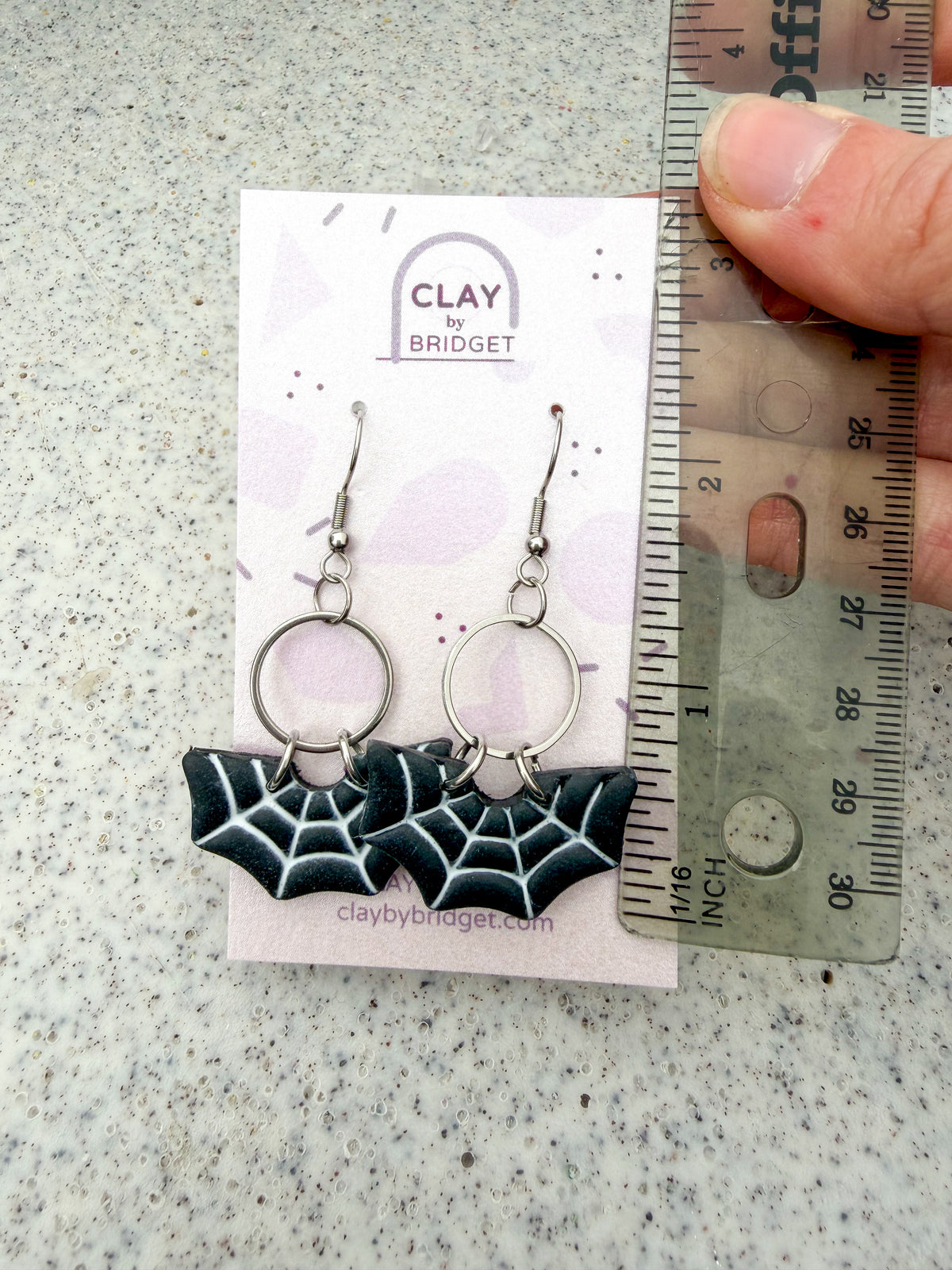 Hand holding earrings next to a ruler for scale. Around 2.25 inches in length. 