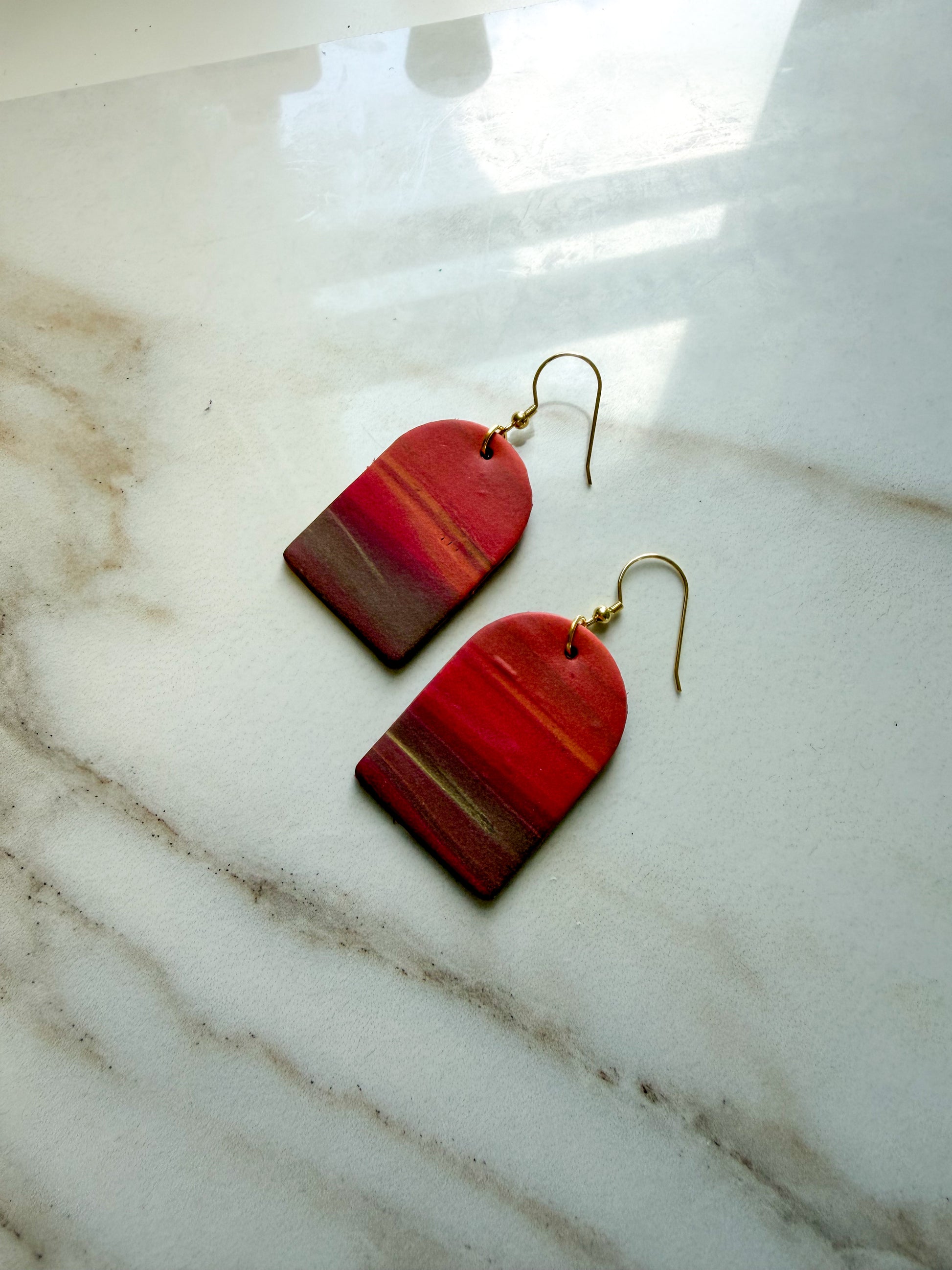 Earrings laying on a marble surface. The design resembles a sunset with colors fading from orange to brown. 