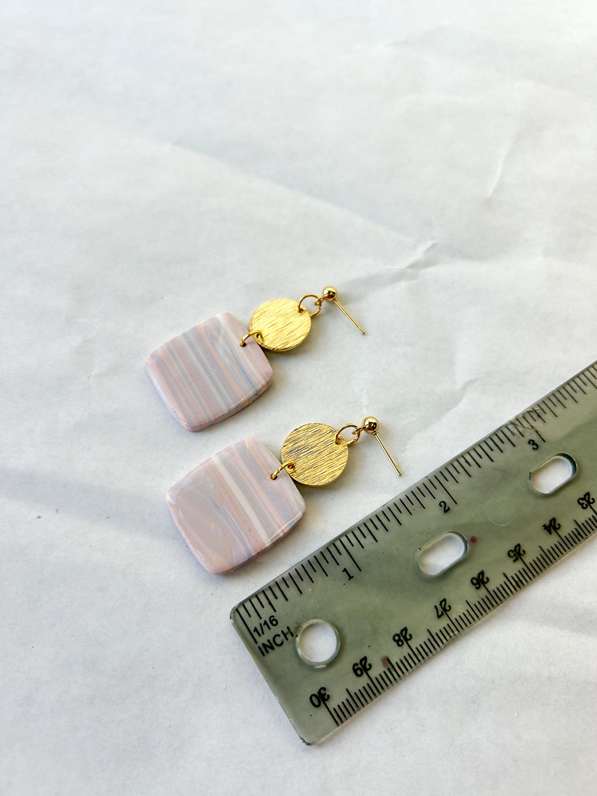 Pair of earrings with pink and gold components next to a ruler on a white background. 2 inches in length