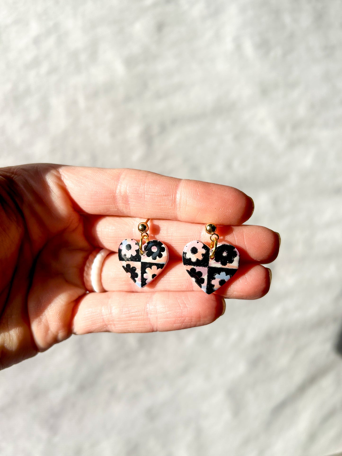 Hand holding a pair of heart dangles with a checker pattern