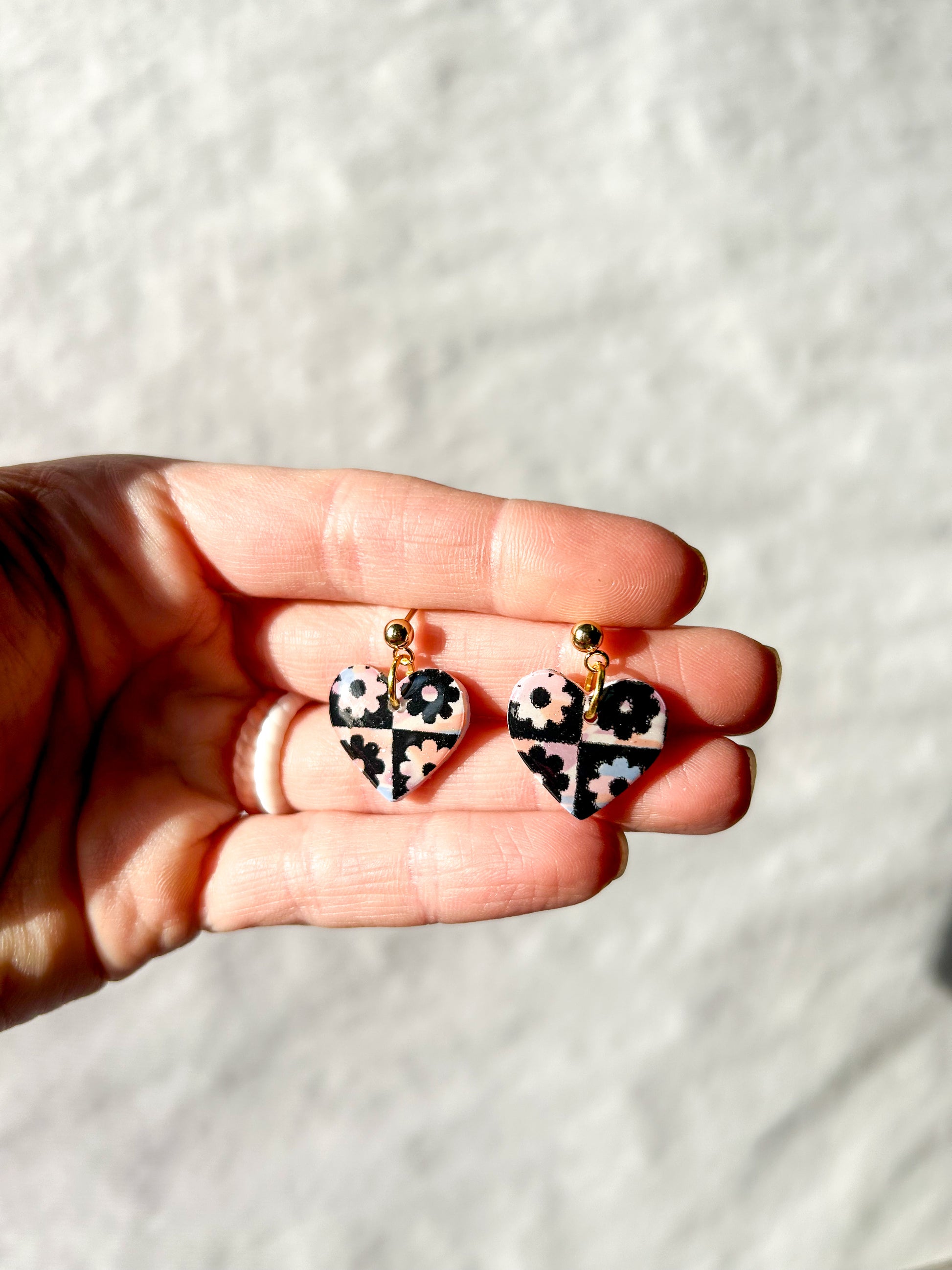 Hand holding a pair of heart dangles with a checker pattern