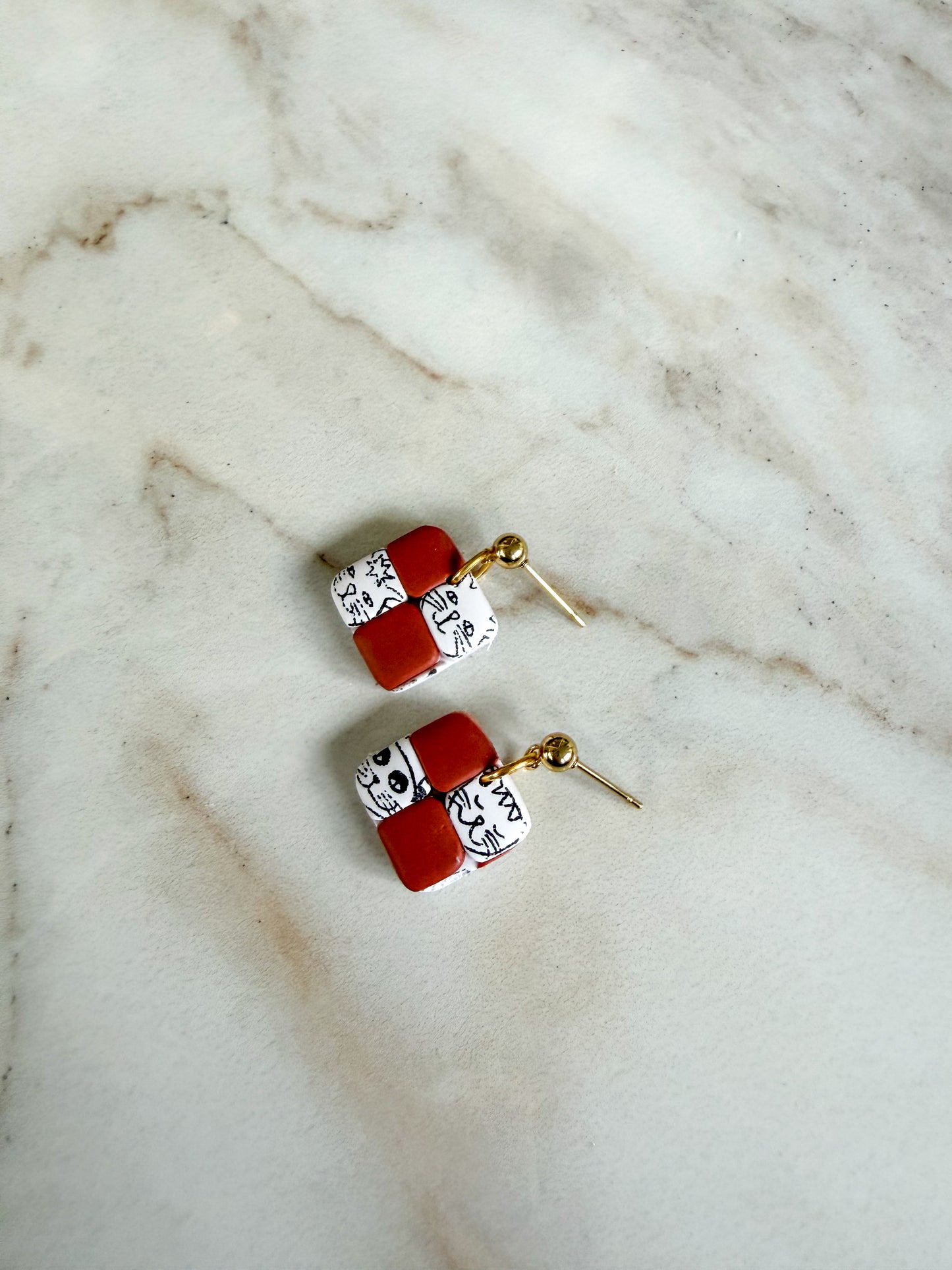 Pair of earrings with terracotta and white square designs on a marble surface