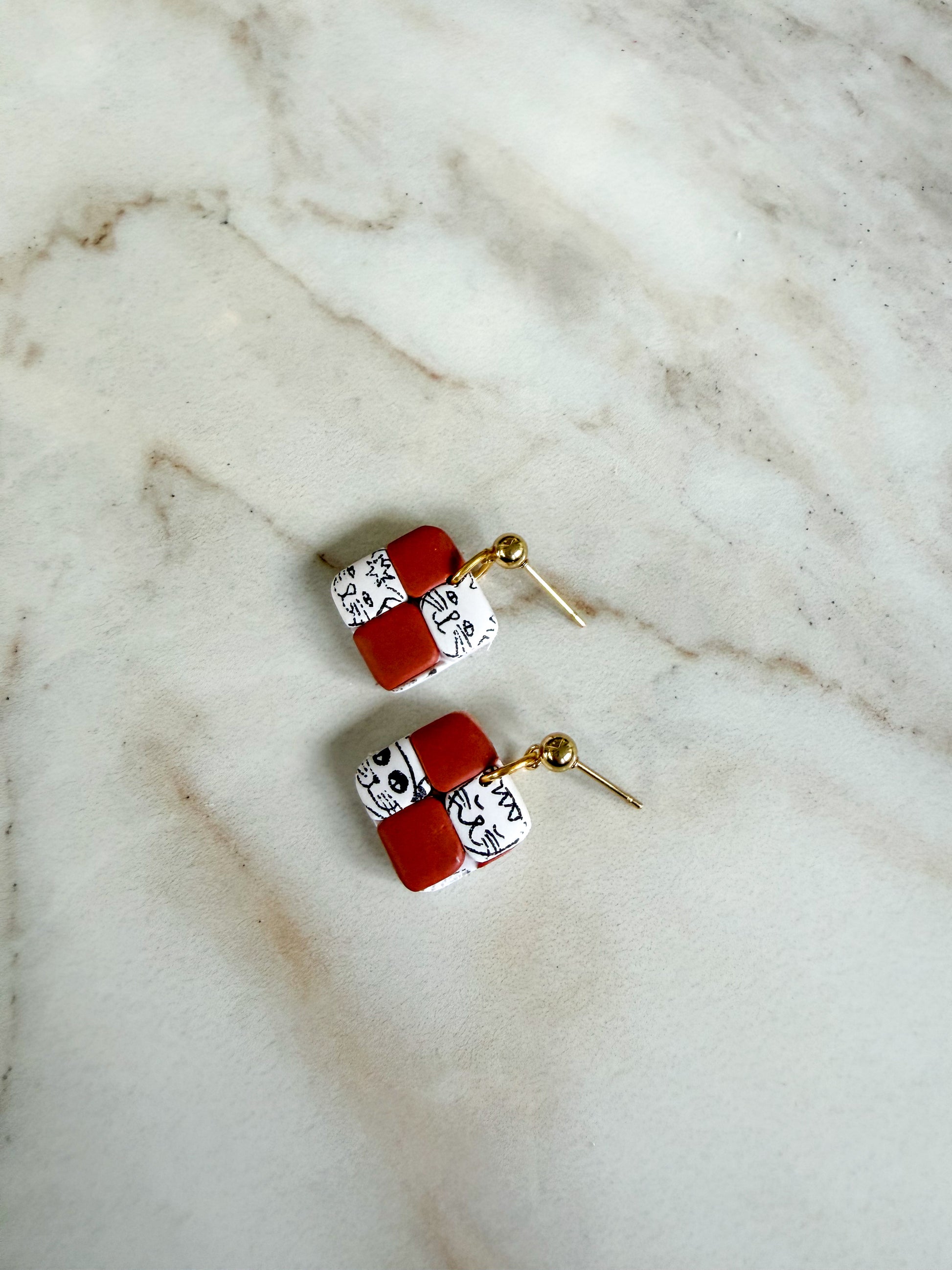 Pair of earrings with terracotta and white square designs on a marble surface