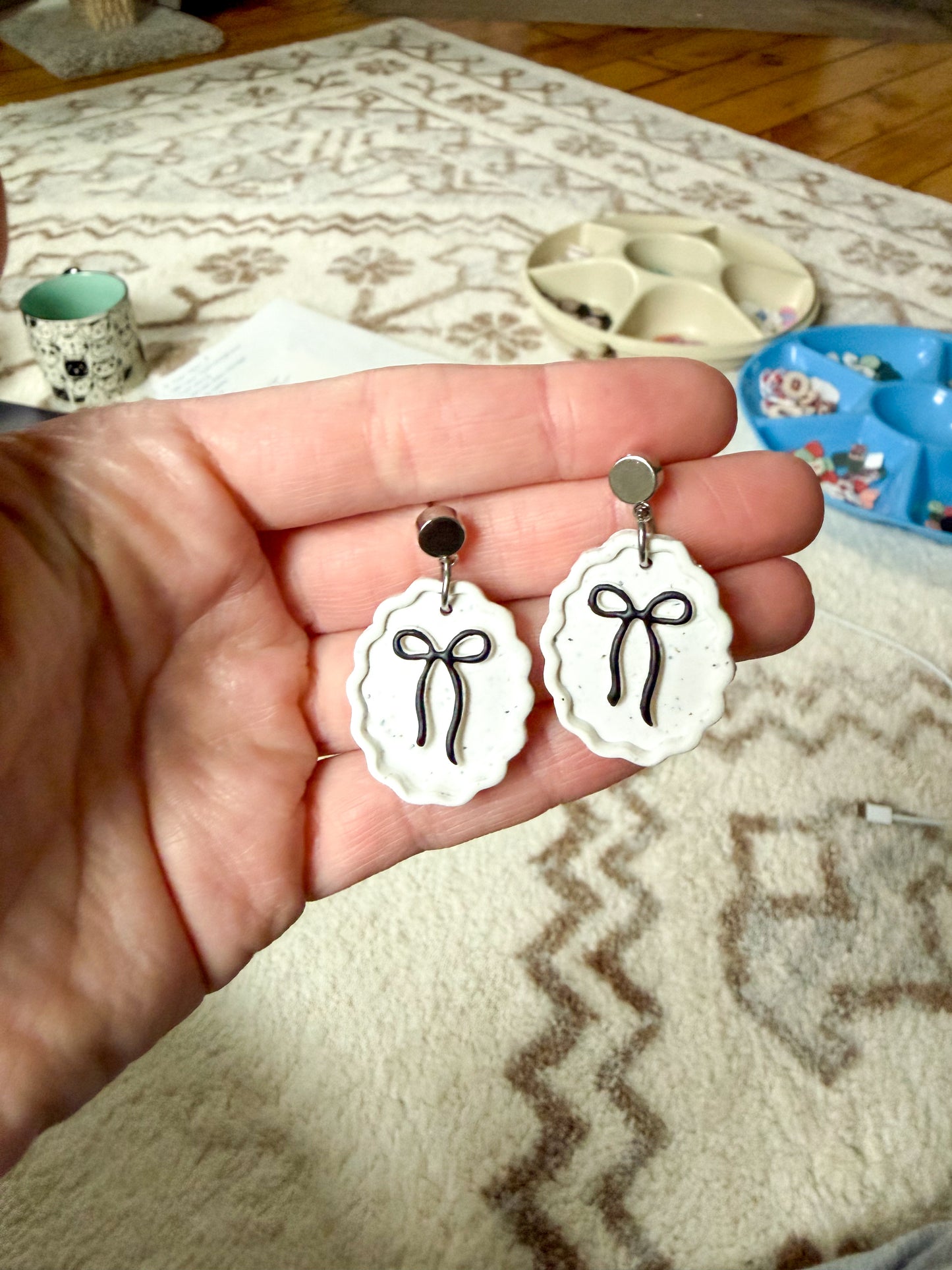 Hand holding a pair of earrings with bow design on a patterned rug.