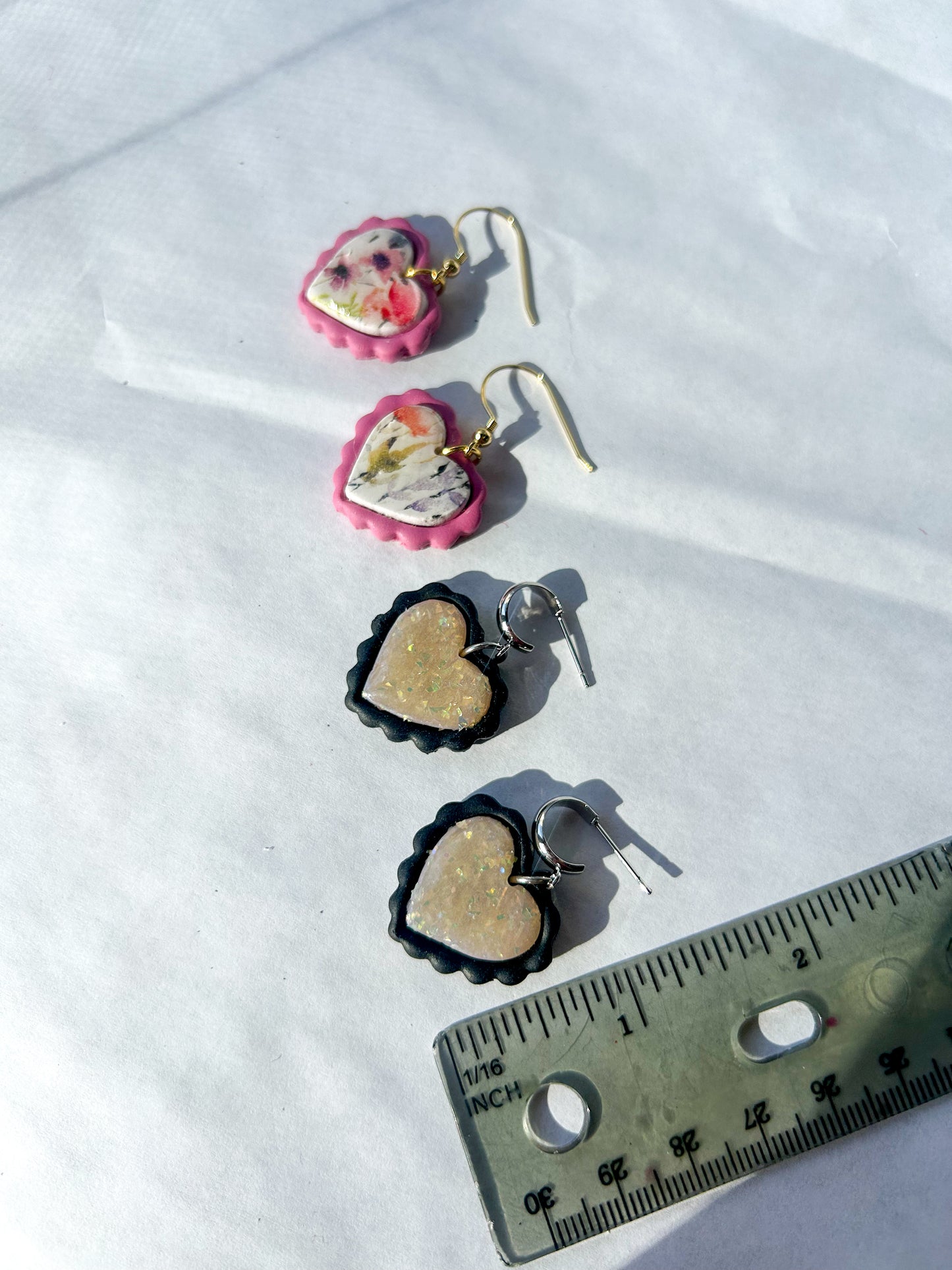 Heart-shaped earrings on a white surface with a ruler for scale. About an inch in length