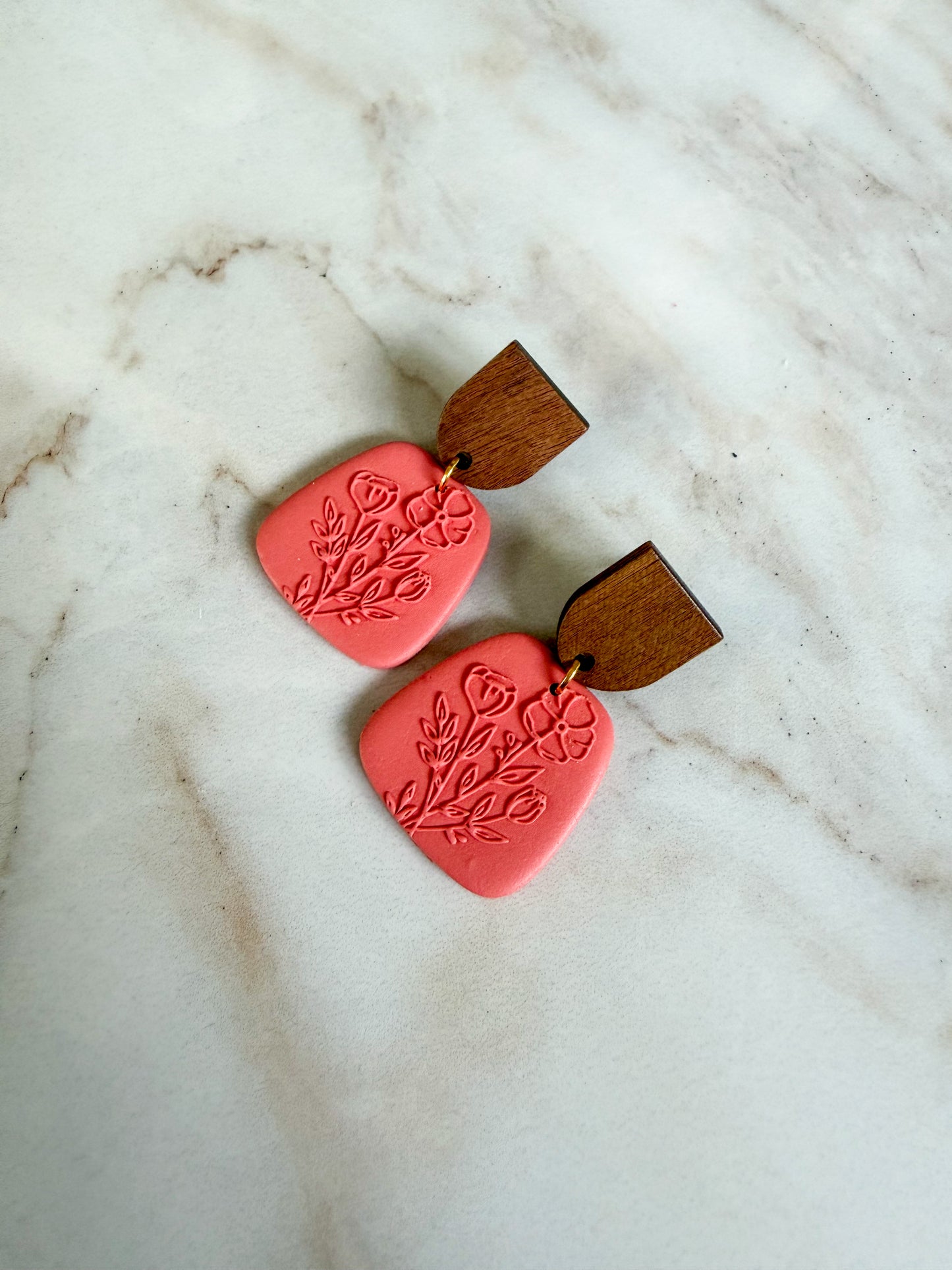 Pair of pink earrings with wooden accents on a marble surface