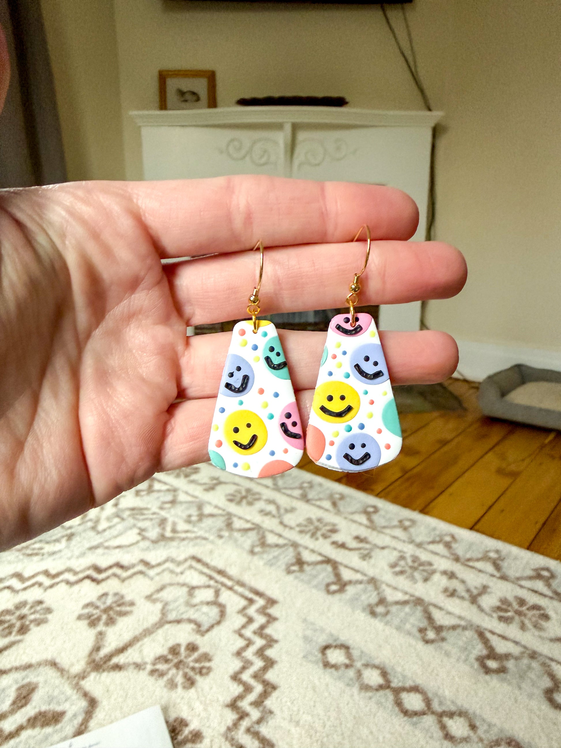 Hand holding colorful smiley face earrings with a neutral background