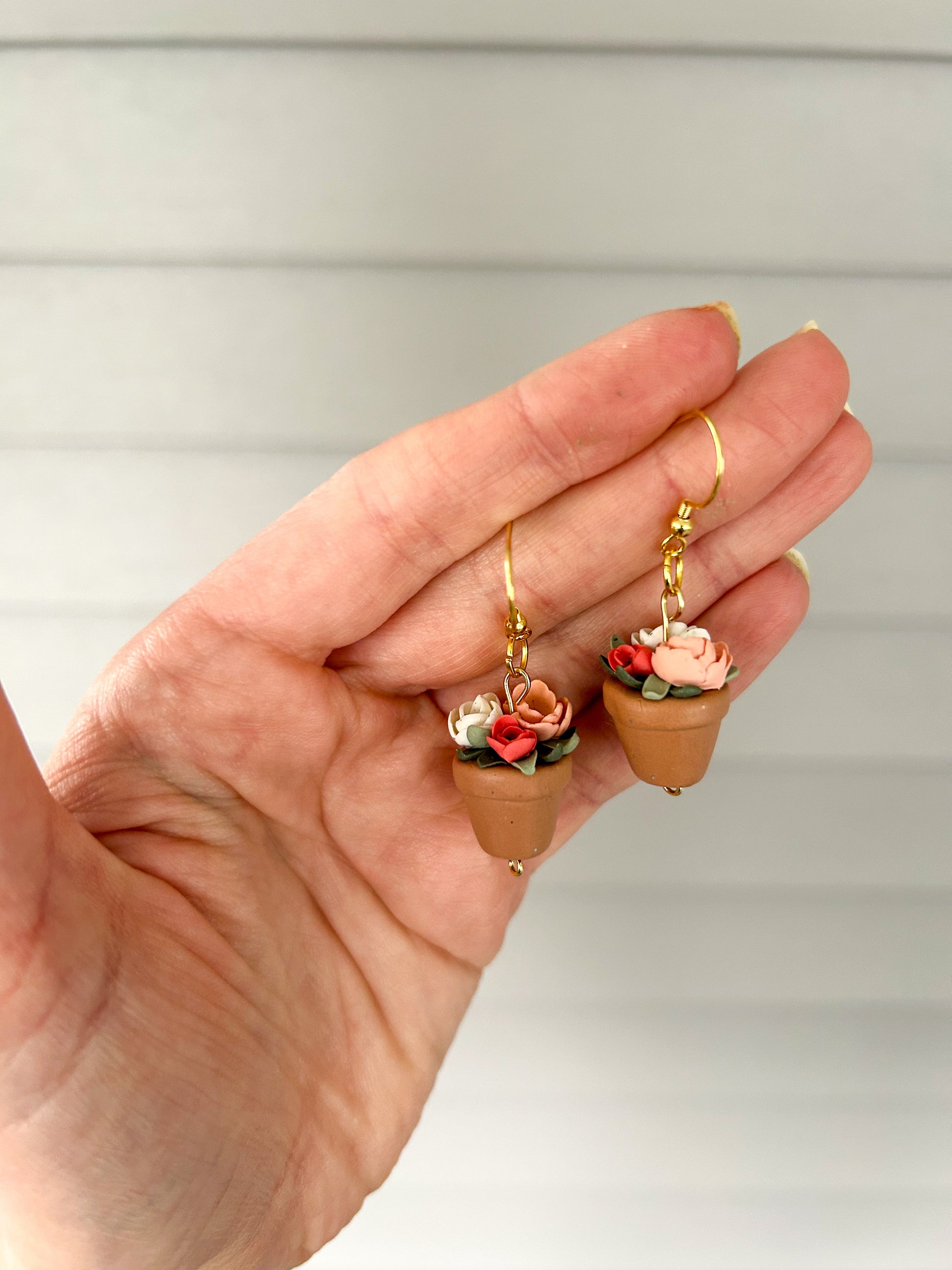 Hand holding a pair of floral earrings with gold hooks against a neutral background