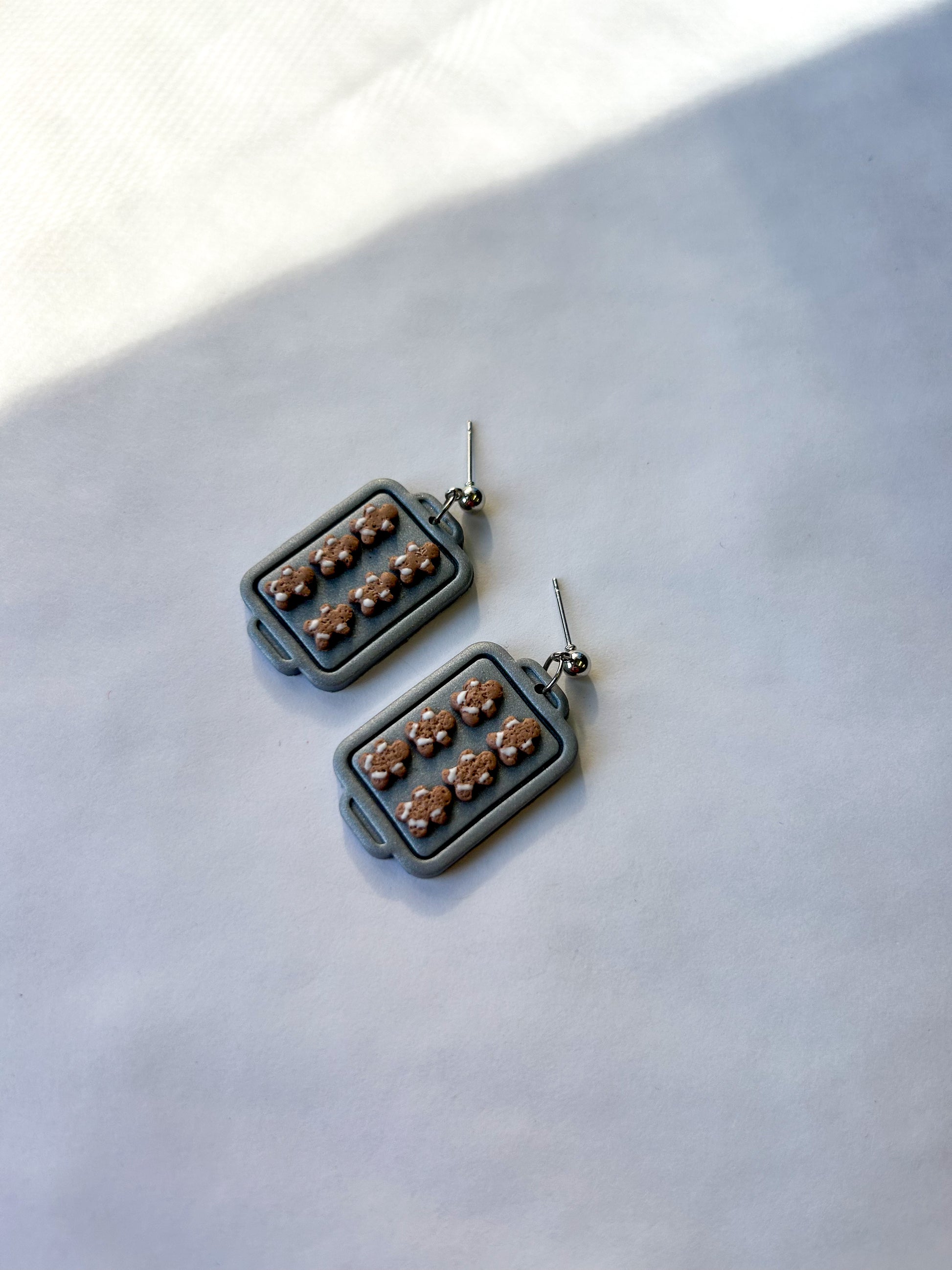 Pair of earrings that are rectangular silver trays with brown gingerbread men on them, sitting on a light background