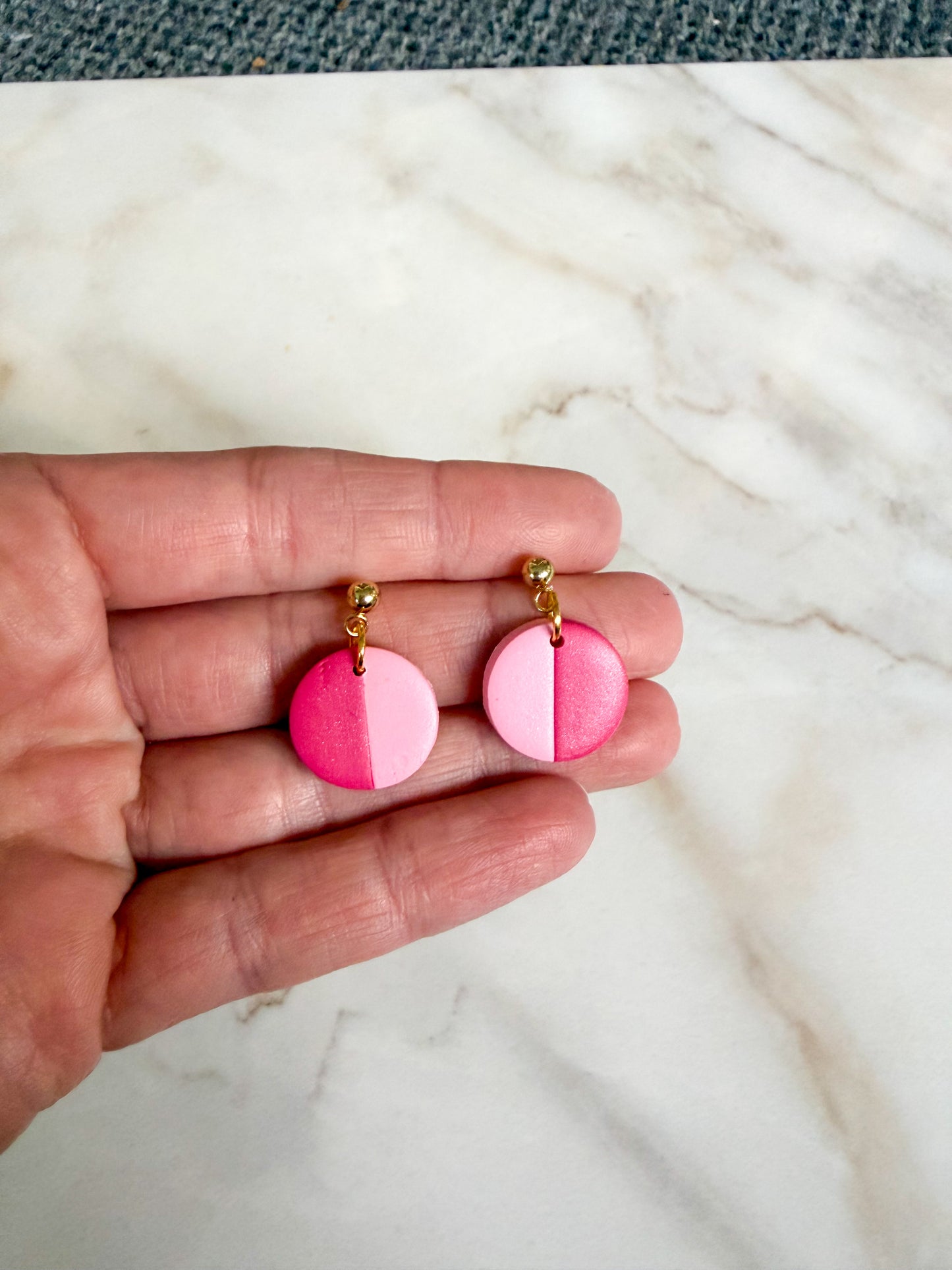 Hand holding pink striped earrings on a marble surface 