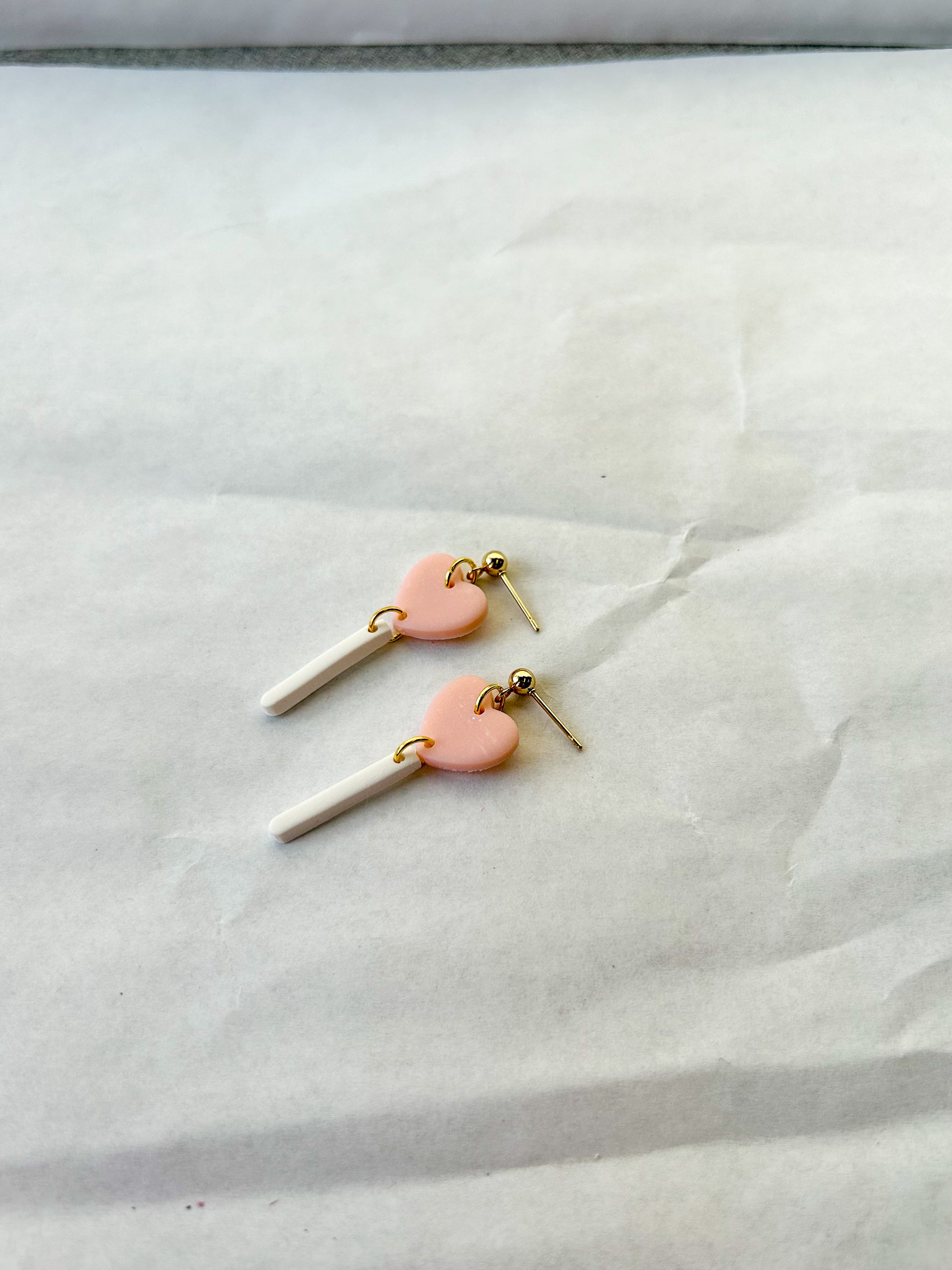 Heart-shaped earrings with pink hearts and white sticks on a white fabric background