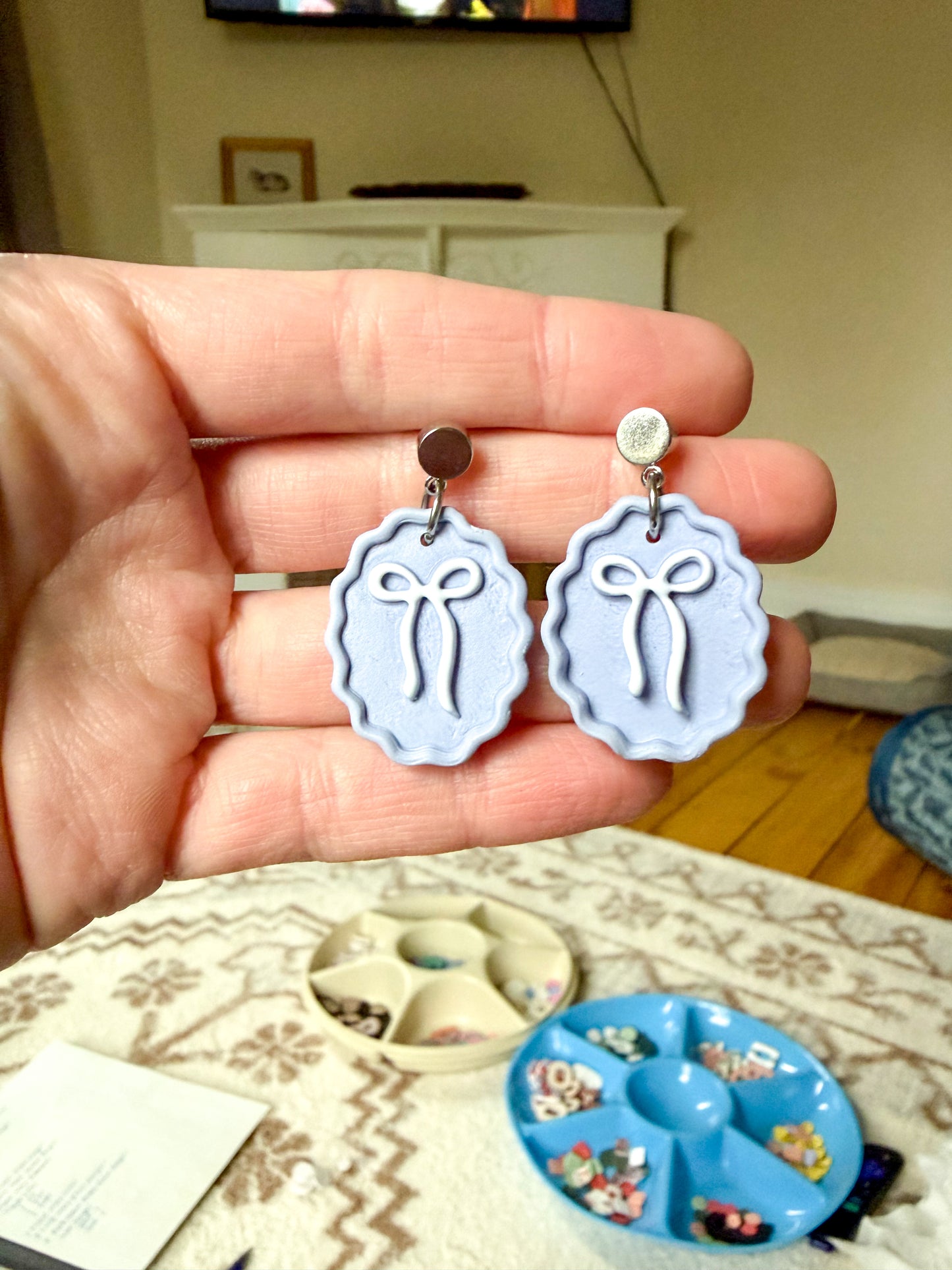 Hand holding a pair of earrings with bow design, with a blurred indoor background.