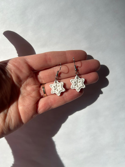 Snowflake earrings held in a hand against a light background