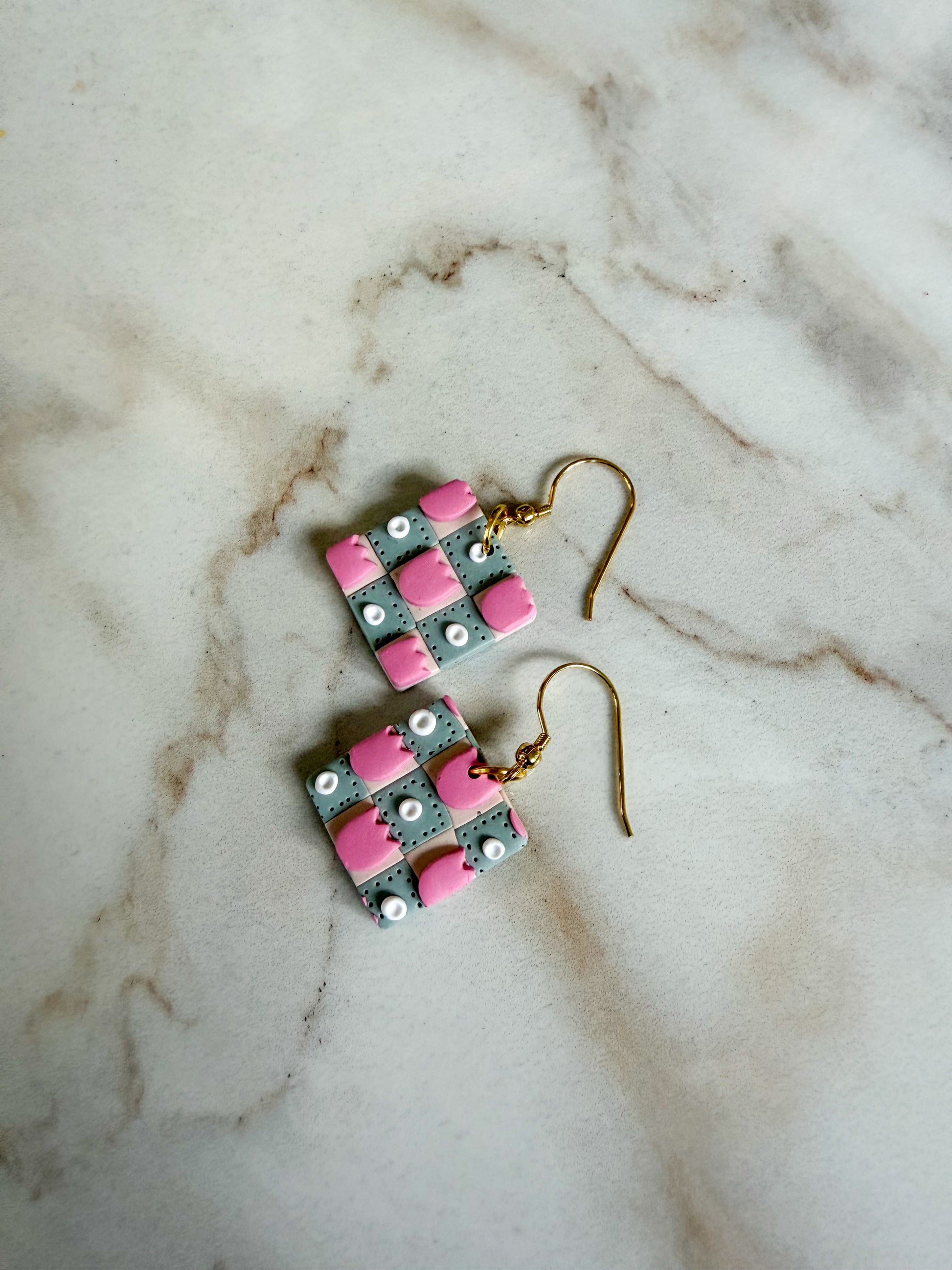 Pair of earrings with pink and green checkered design on a marble surface