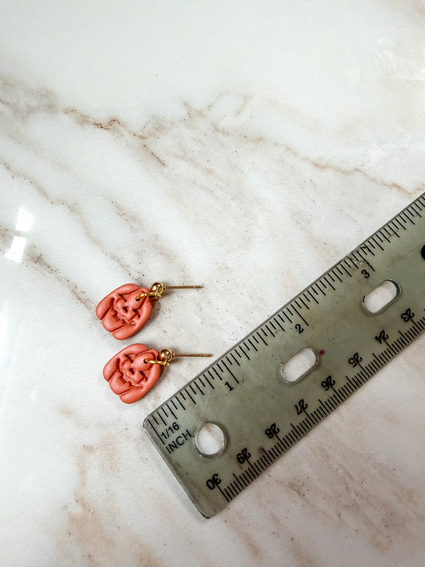 A pair of dangle earrings with gold-tone posts, displayed next to a ruler on a white marble surface to show scale. About 1 inch long 