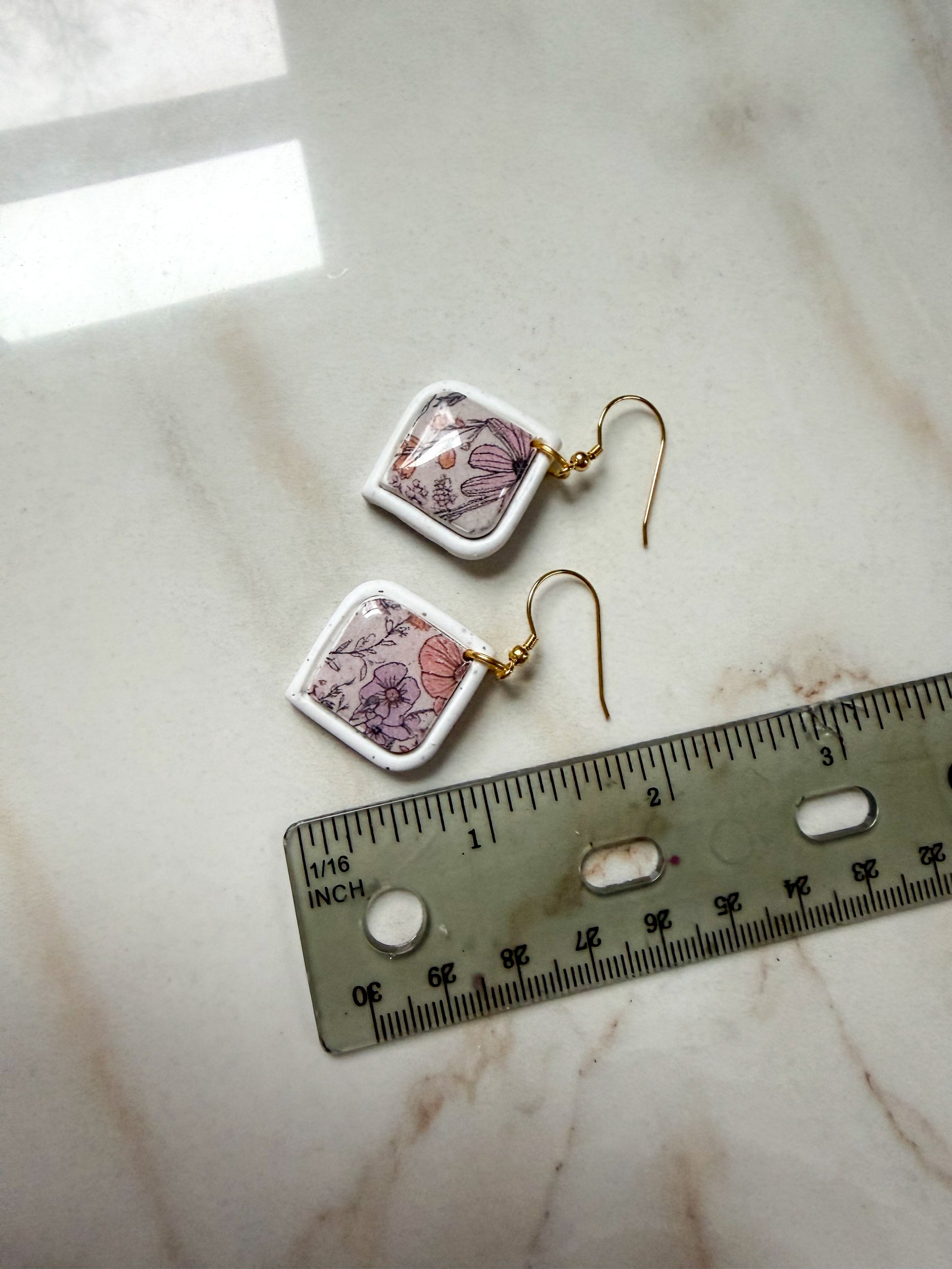 Pair of floral earrings on a marble surface with a ruler for scale. A little under 2 inches in length. 