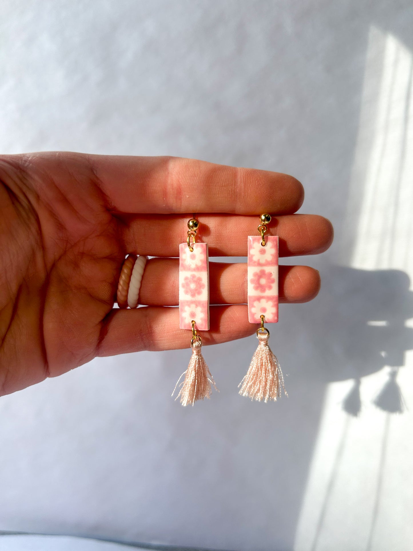 Hand holding pink beaded earrings with tassels against a white background