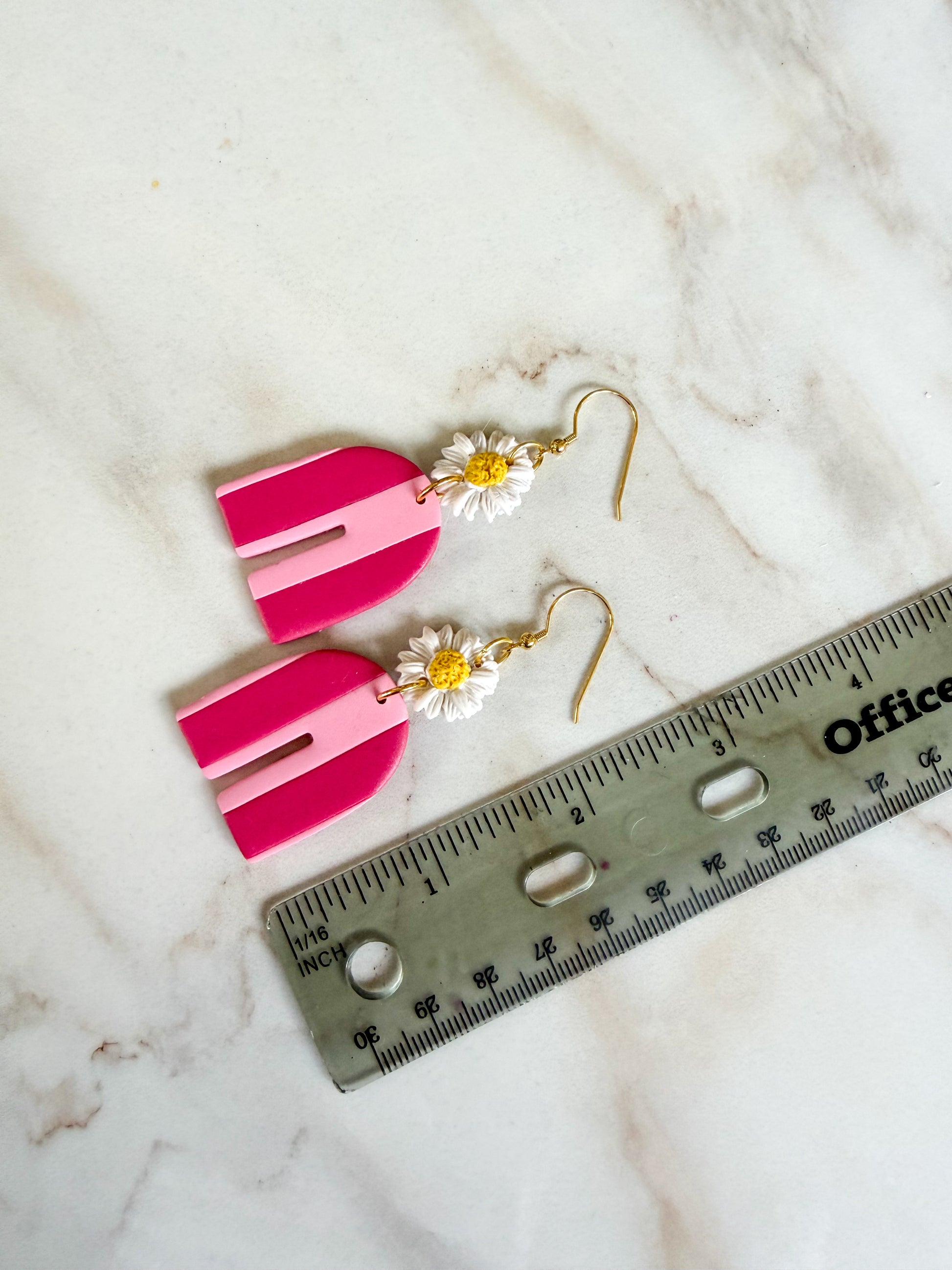 Pink earrings with flowers on a marble surface next to a ruler for scale. Nearly 3 inches in length. 