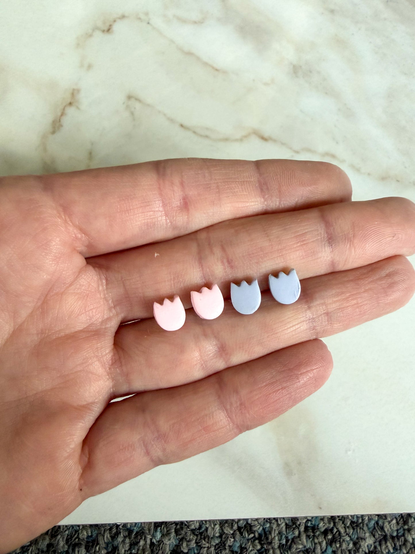 Tulip stud earrings between fingers on a marble surface 
