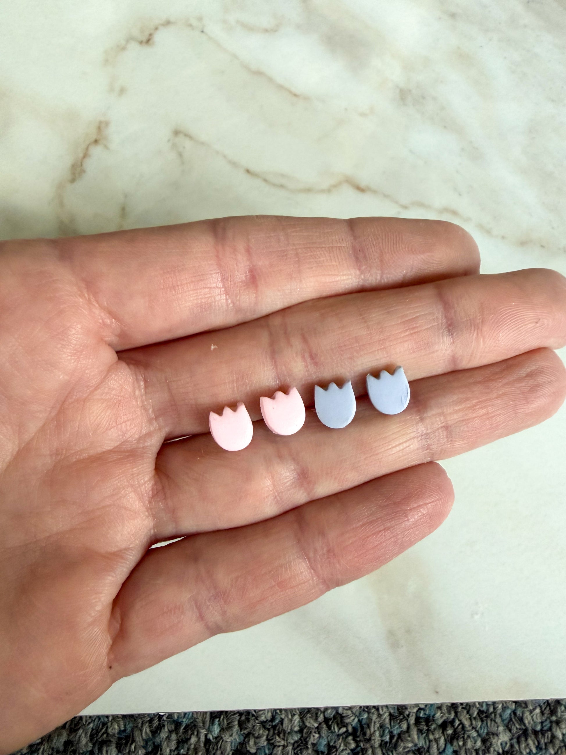 Tulip stud earrings between fingers on a marble surface 