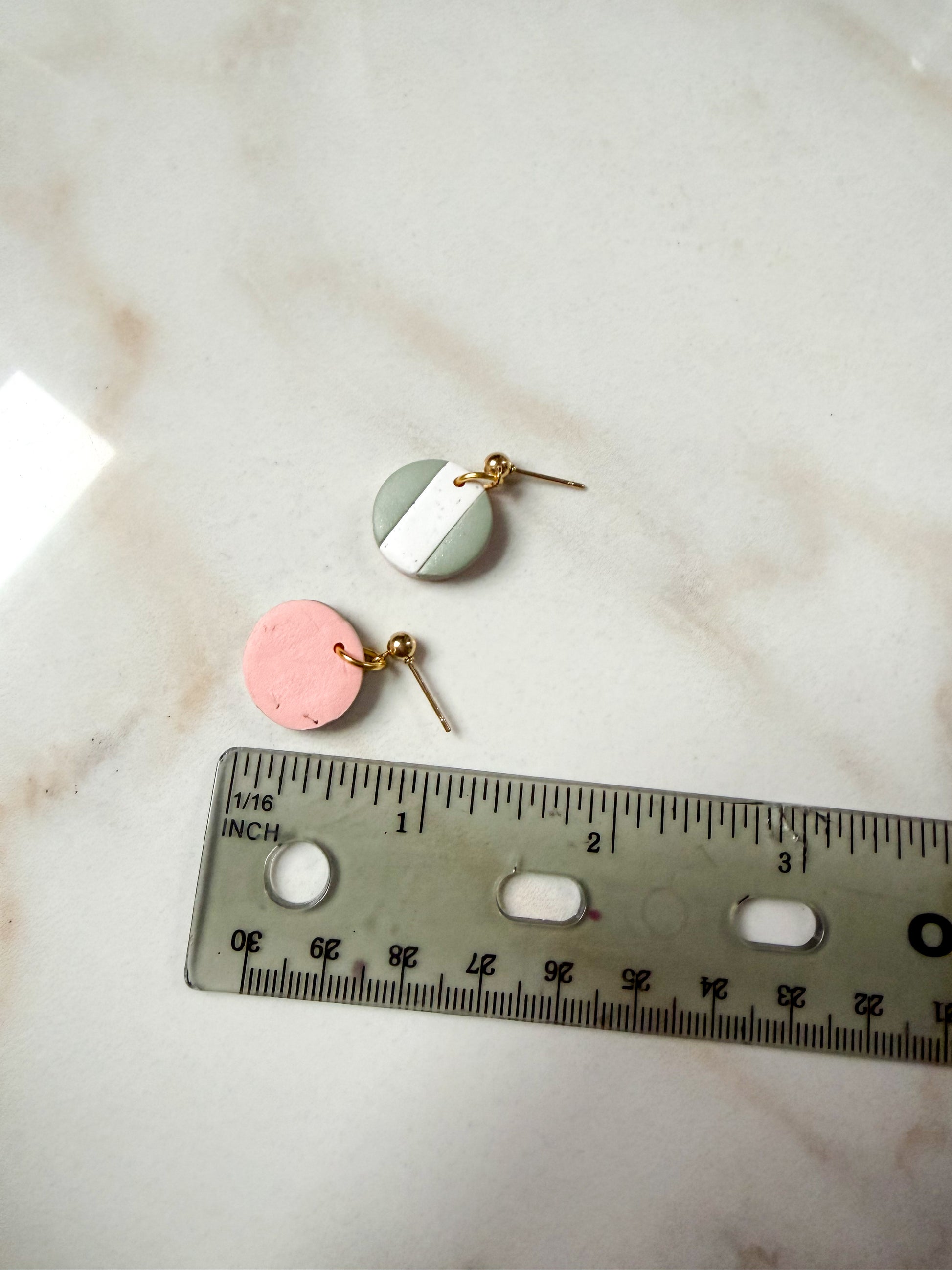 Pair of earrings on a marble surface with a ruler for scale. About an inch long 