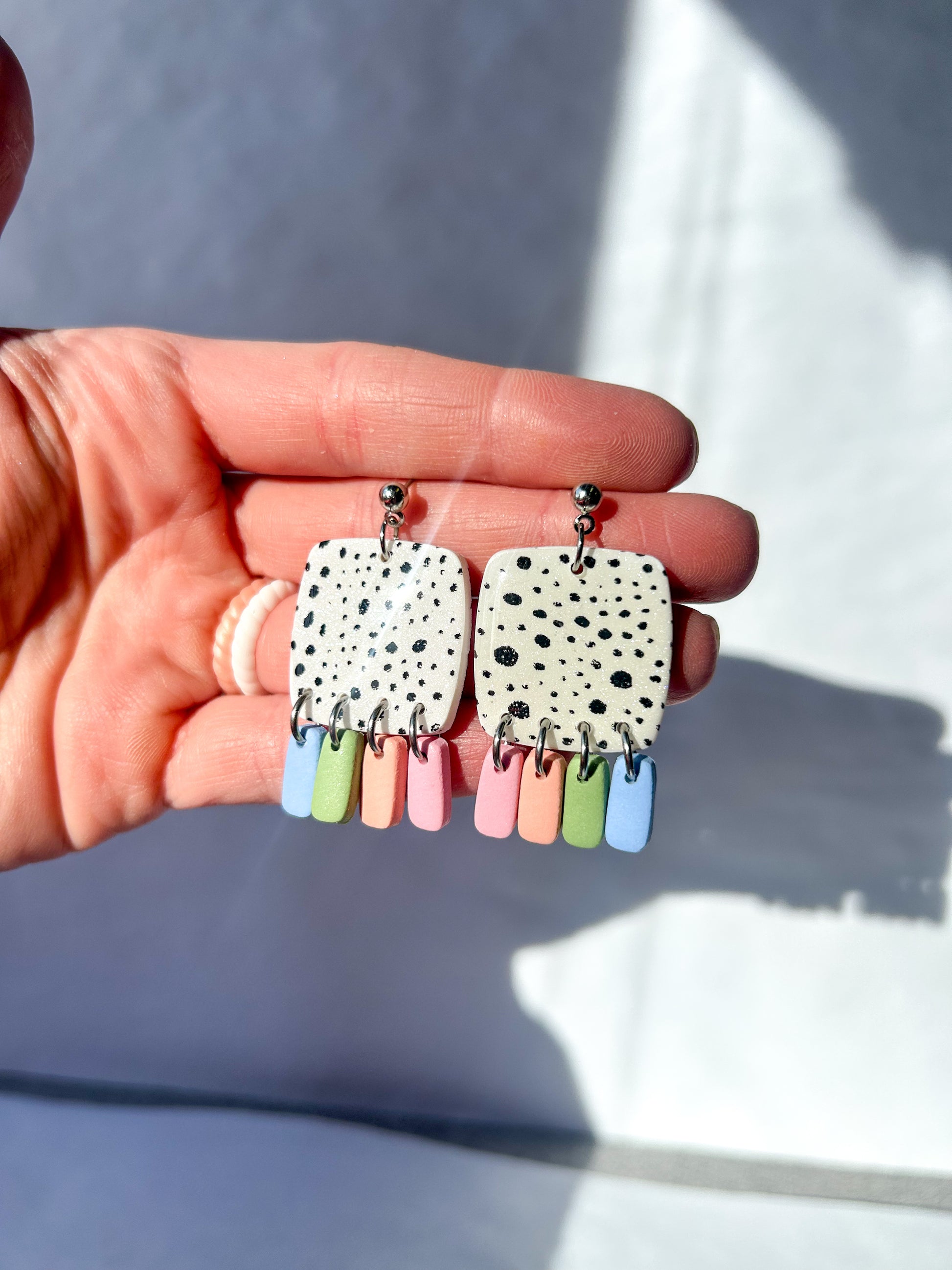 Hand holding a pair of earrings with spotted design and colorful dangling elements.