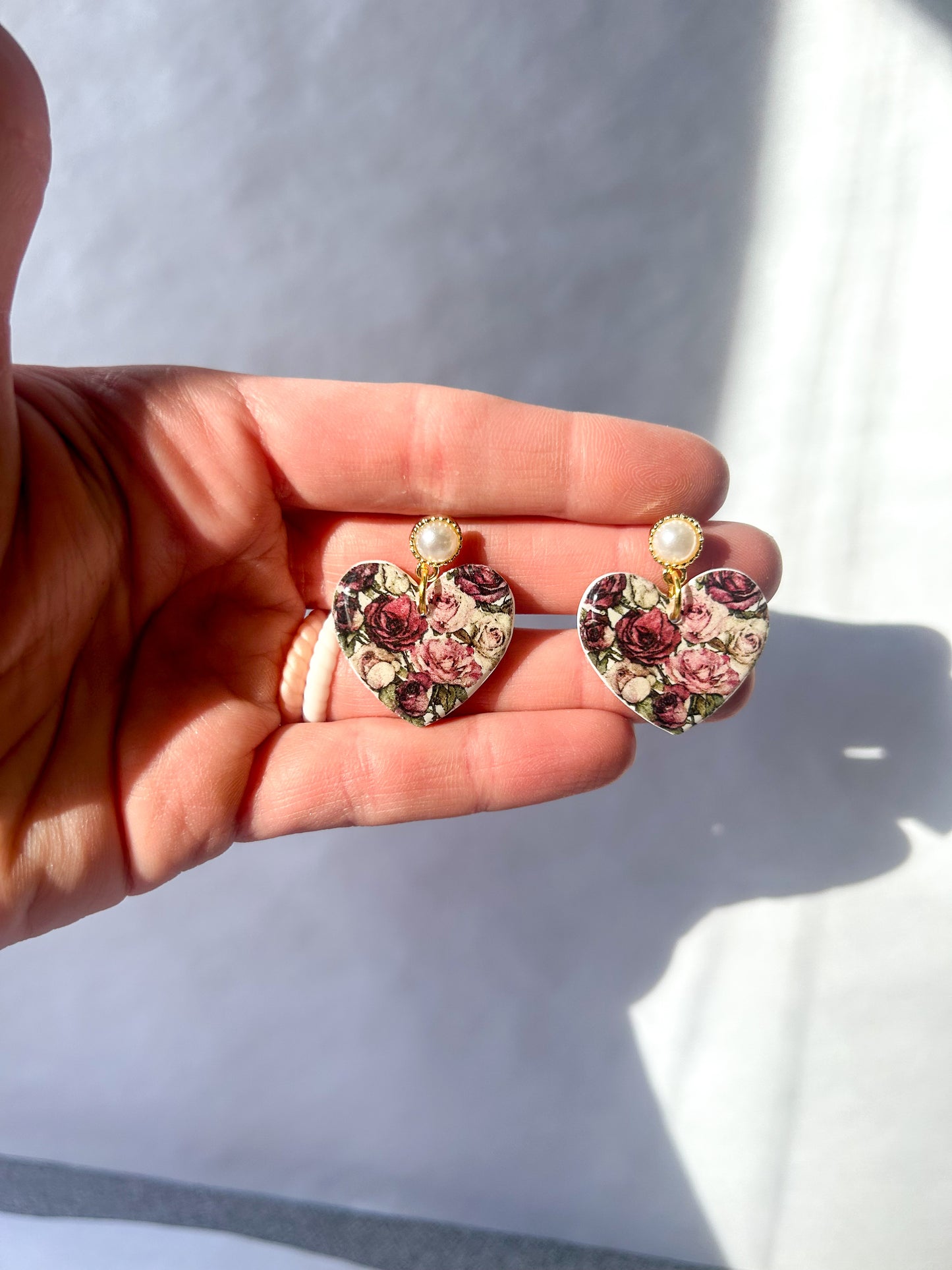 Heart-shaped earrings with floral design held in a hand against a white background