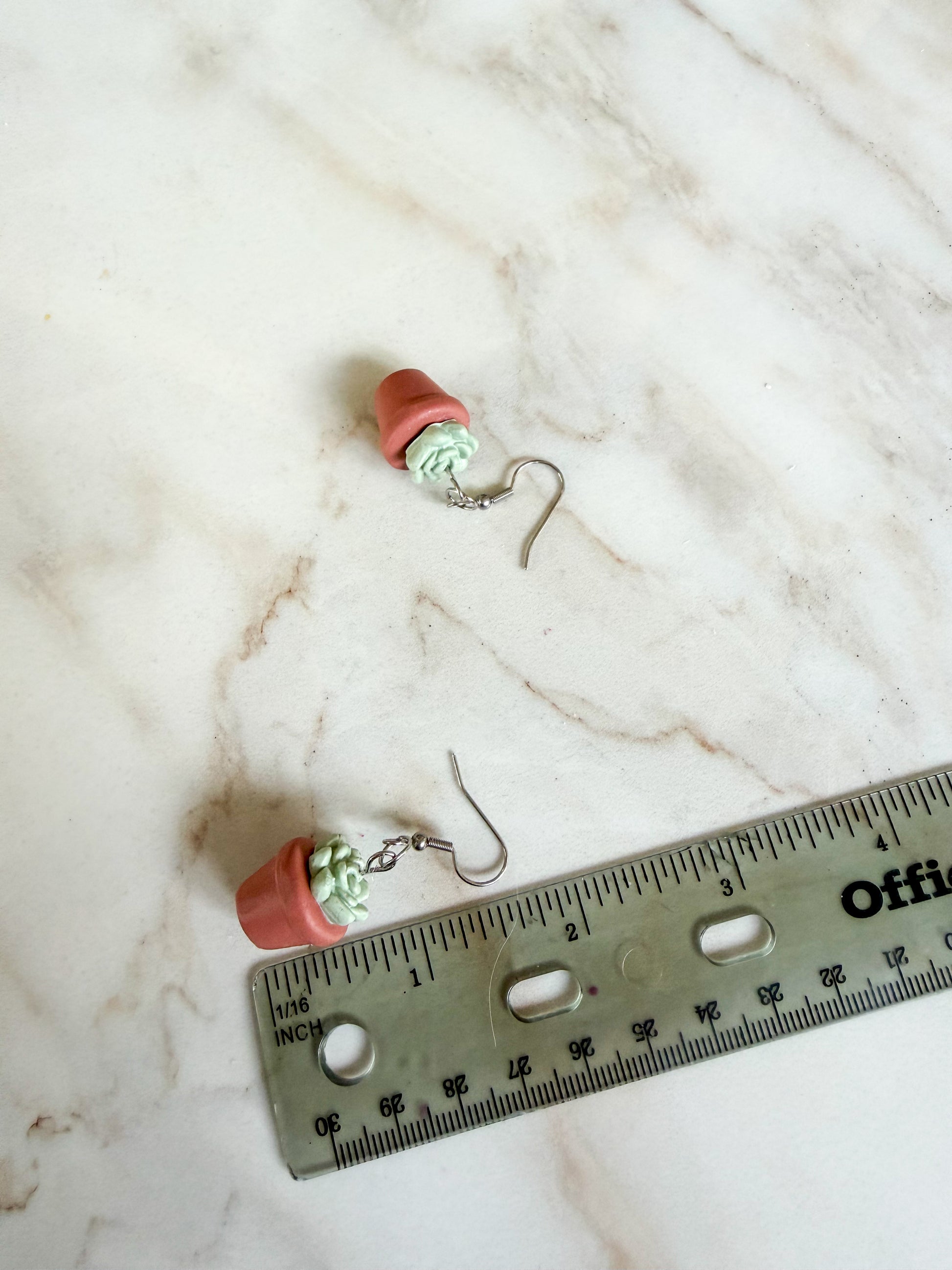 Small pink earrings with green beads on a marble surface next to a ruler for scale. A little under 2 inches long 