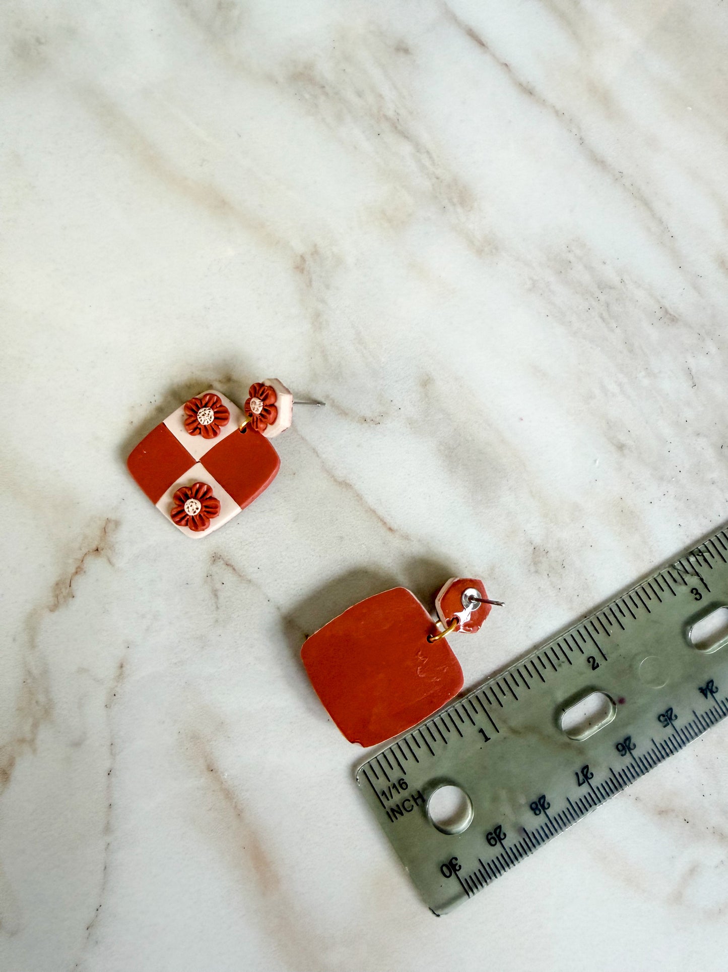 Two earrings on a marble surface with a ruler for scale. About an inch and a half in length 