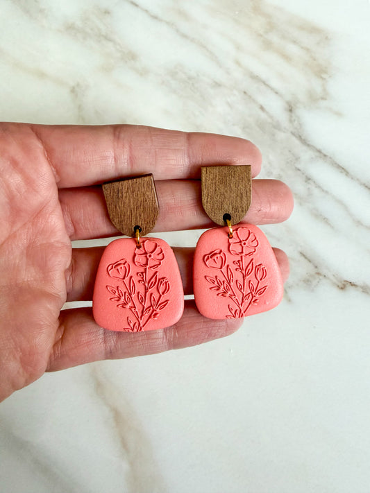Pink earrings with wooden tops held between fingers on a marble background