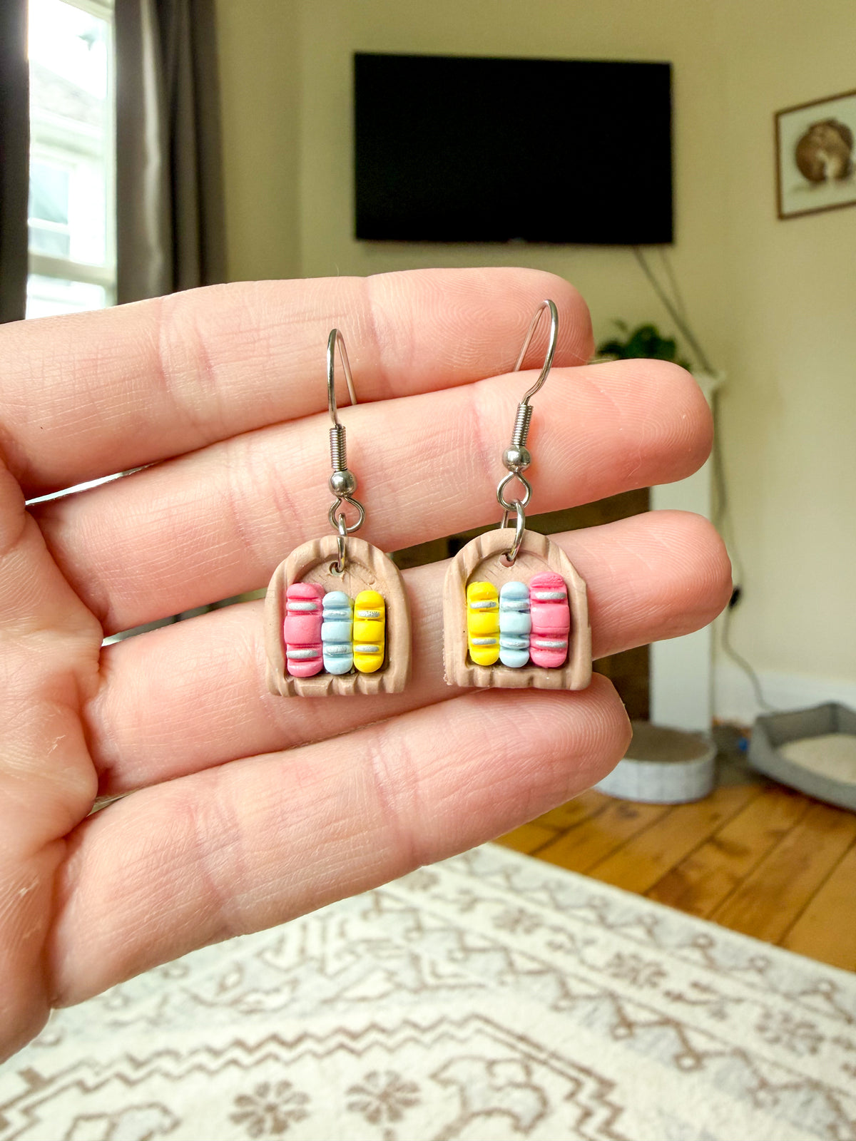 Hand holding a pair of earrings that resemble a small bookshelf. 