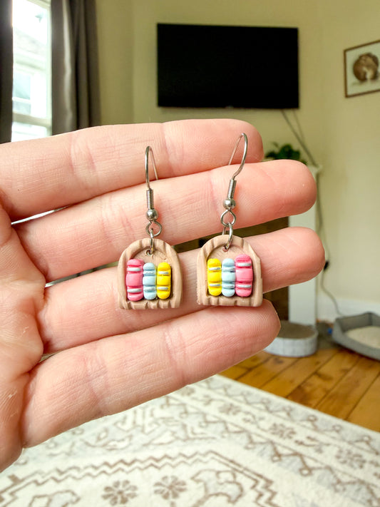Hand holding a pair of earrings that resemble a small bookshelf. 