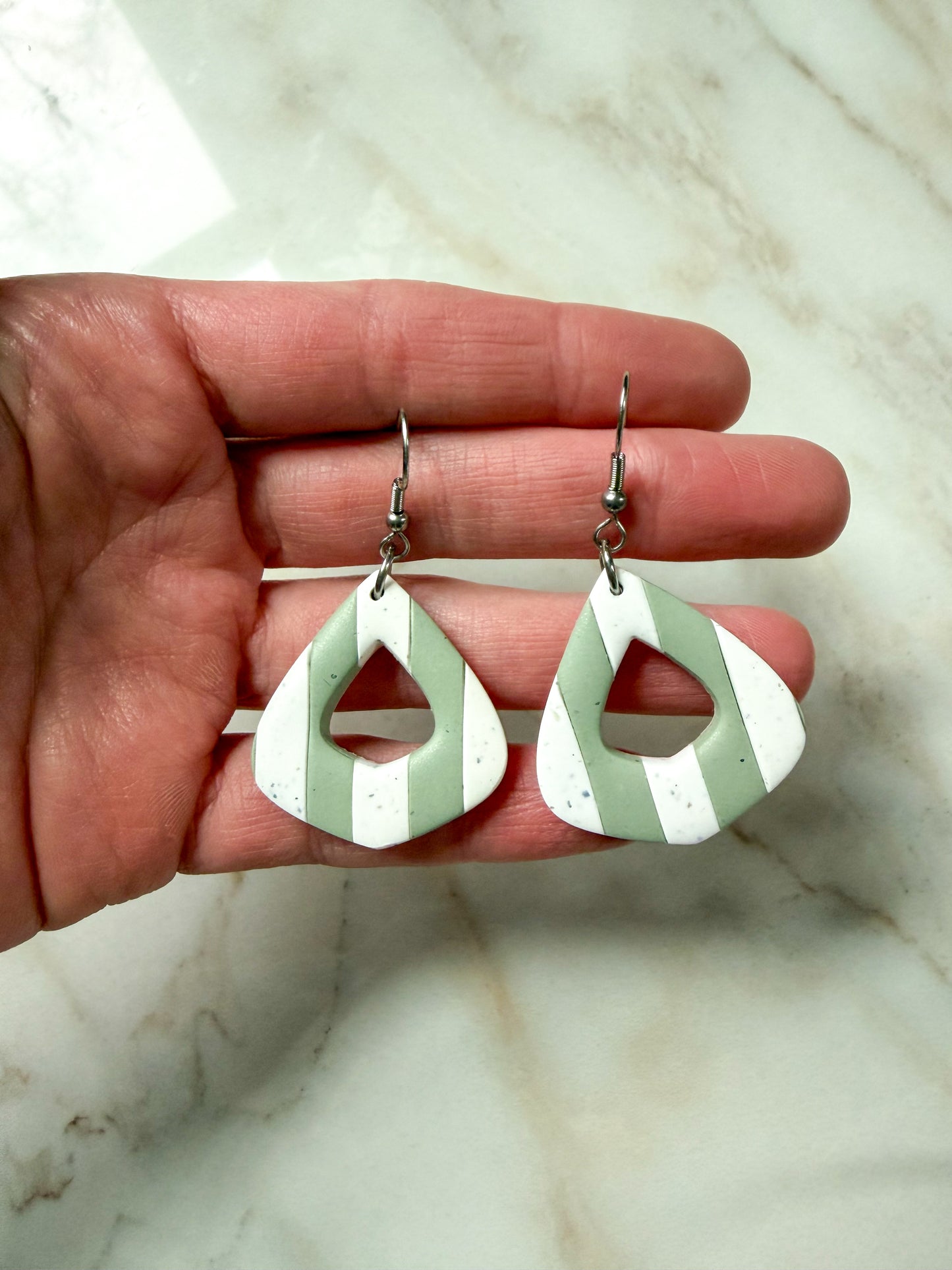 Green and white striped earrings held in a hand against a marble background