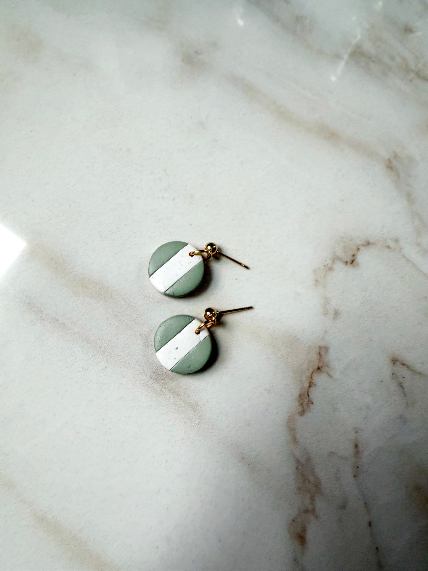 Pair of green and white circular earrings on a marble surface