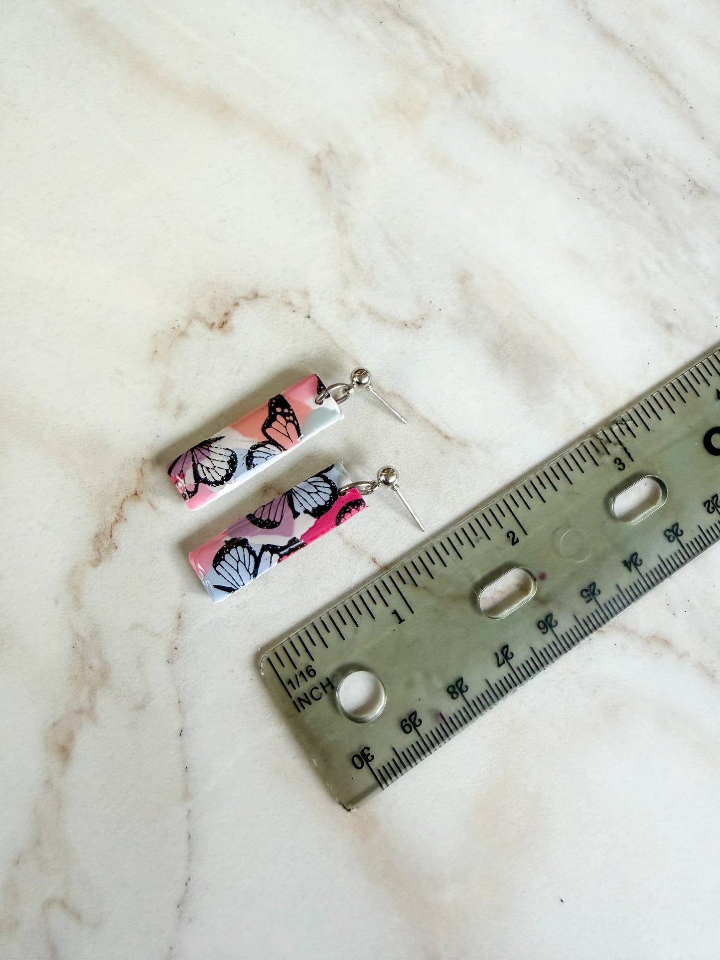 Butterfly-patterned earrings on a marble surface with a ruler for scale. About one and a half inches long 