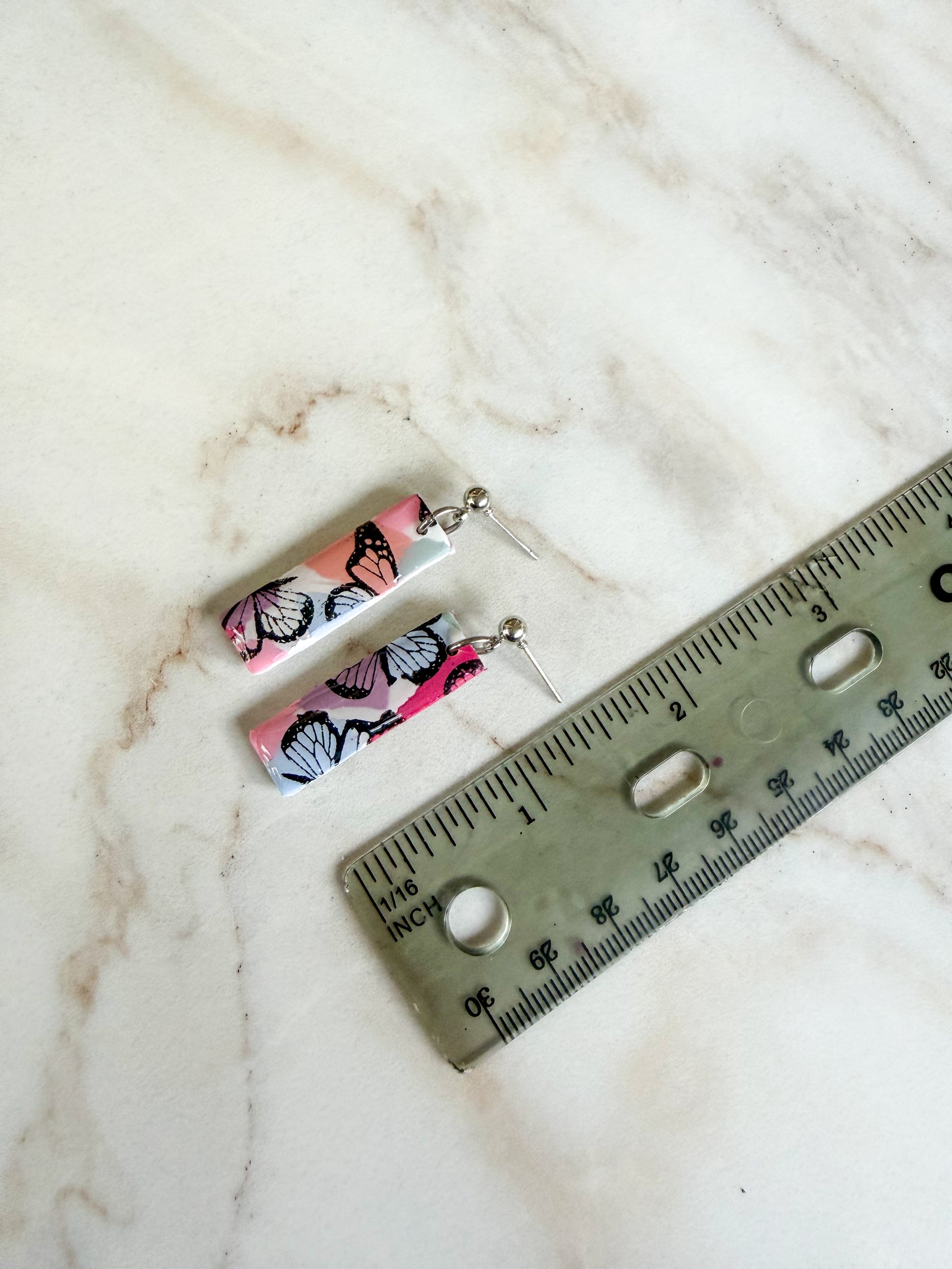 Butterfly-patterned earrings on a marble surface with a ruler for scale. About one and a half inches long 