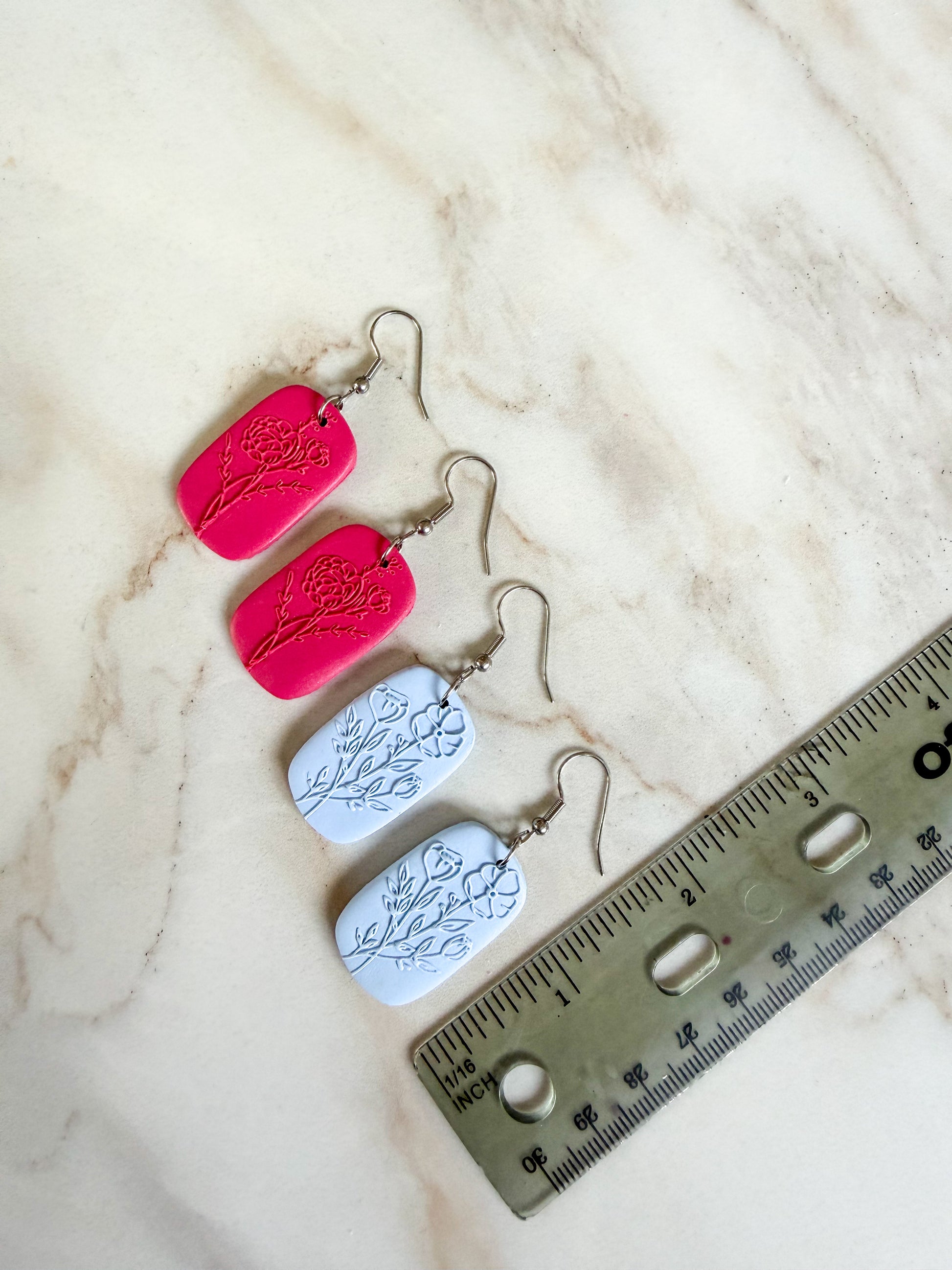 Earrings with leaf designs on a marble surface next to a ruler for scale. About 2 inches long 