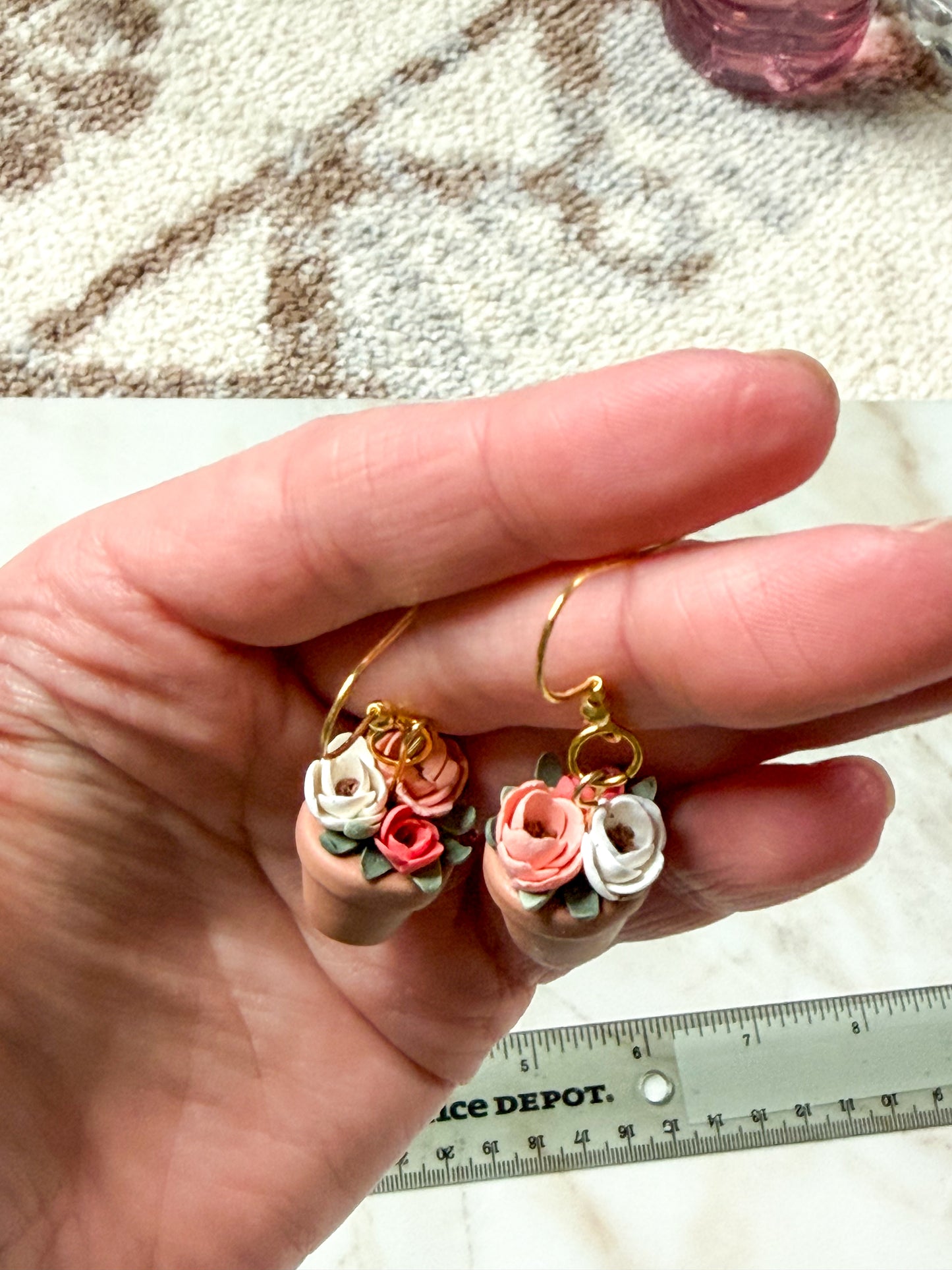 Hand holding a pair of floral earrings.