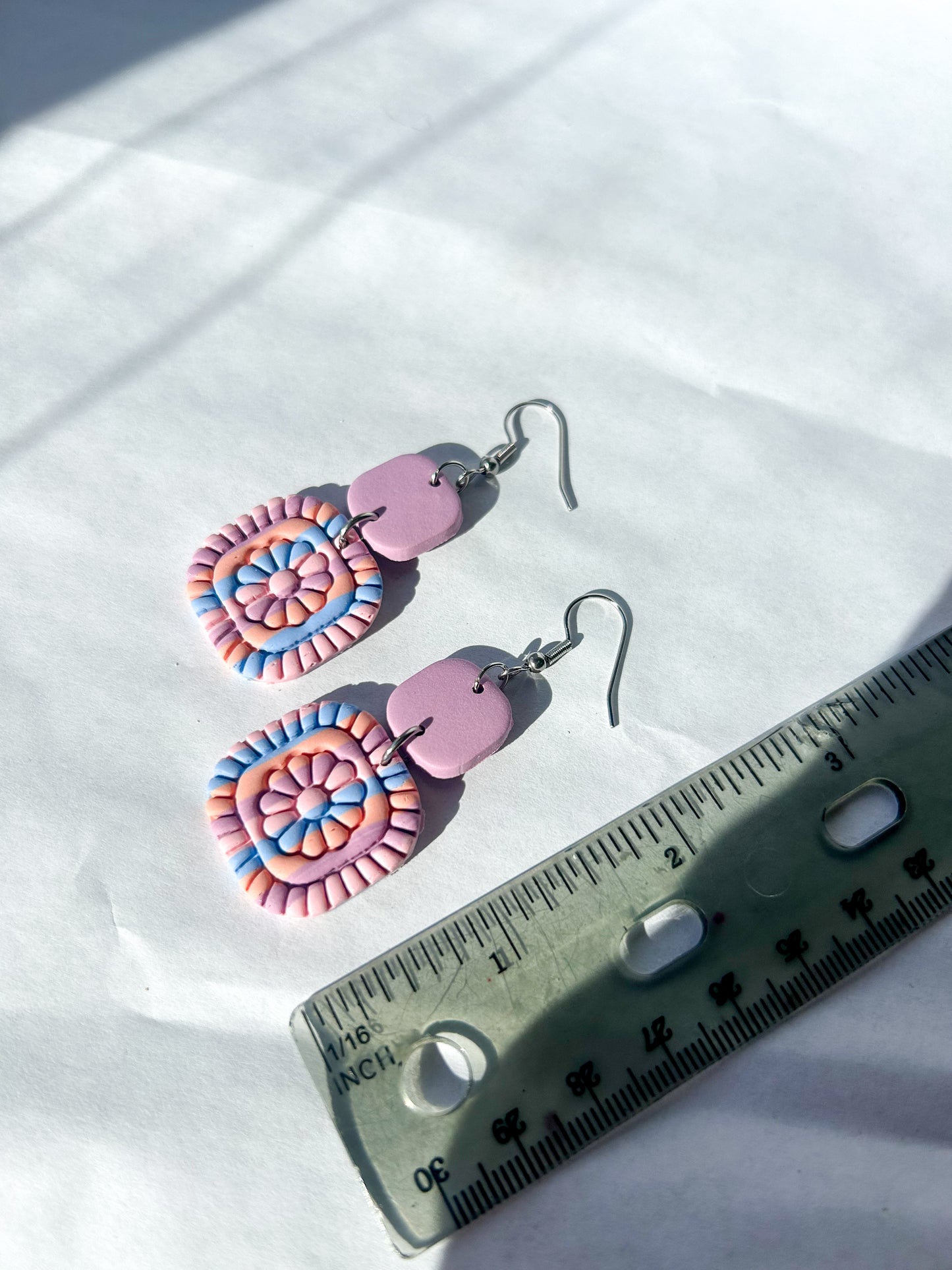 Colorful spiral earrings with a ruler for scale on a white background