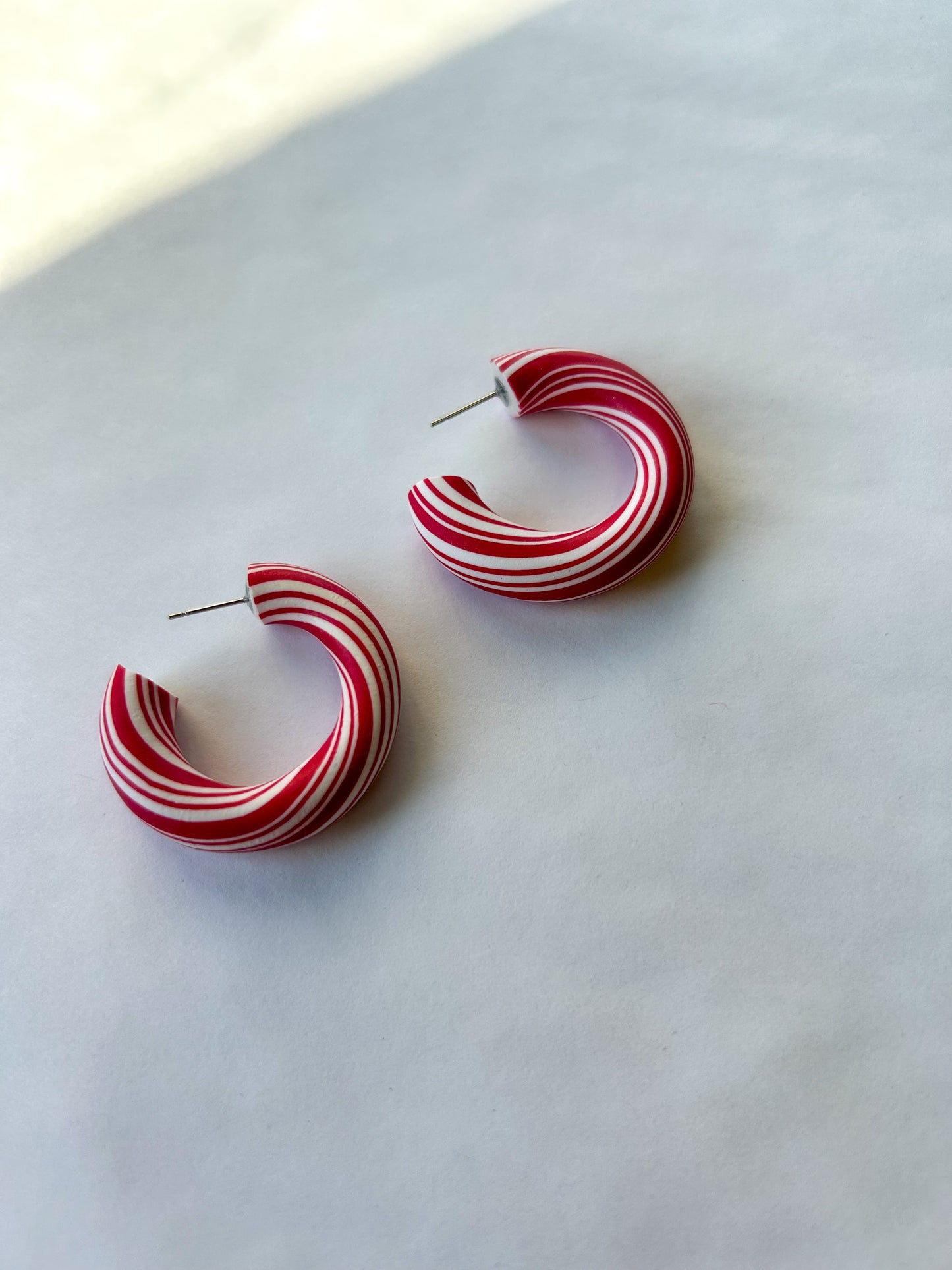 Red and white peppermint striped hoop earrings on a light background