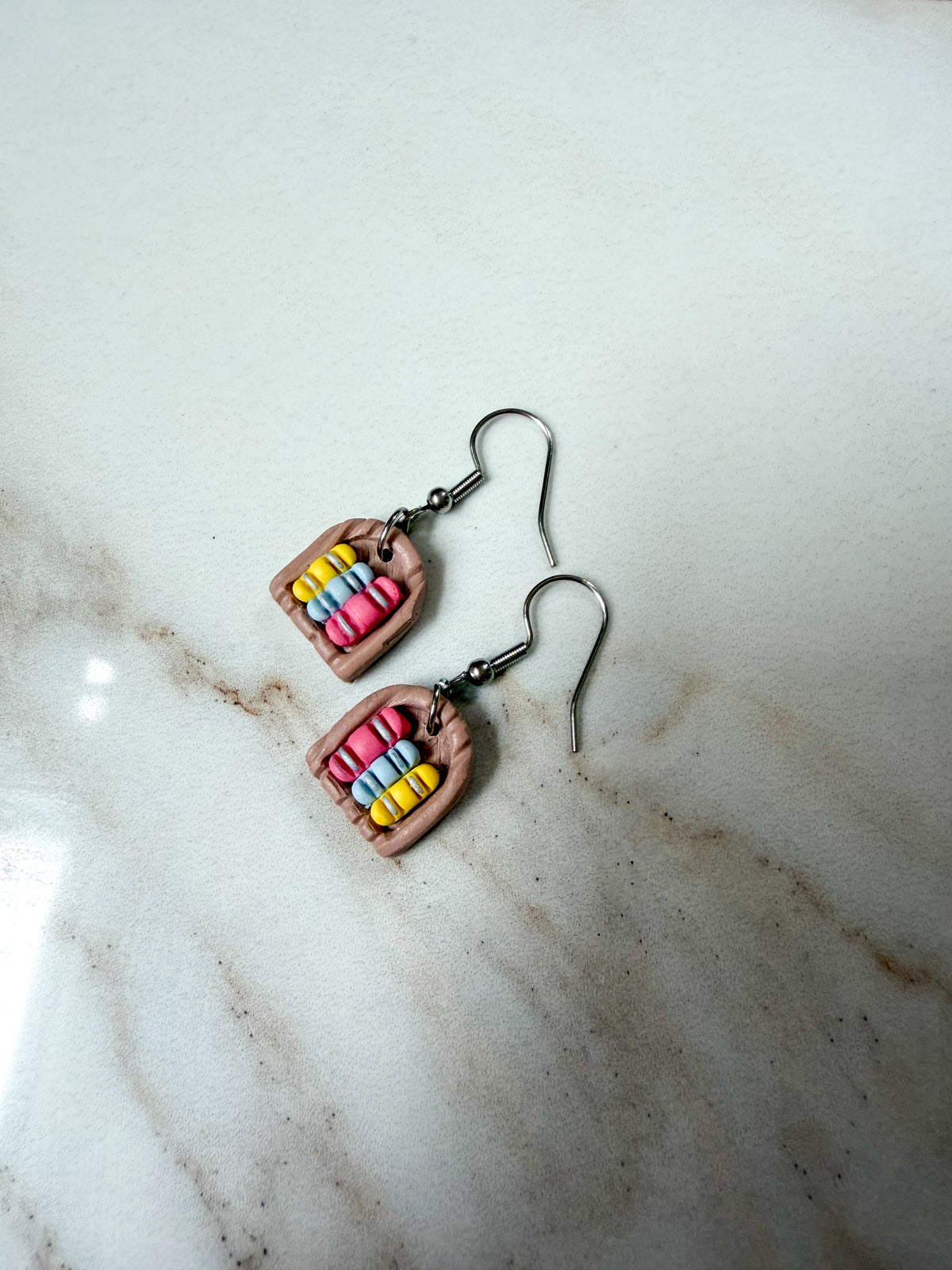 Earrings lying on a marble surface. They resemble a small arched bookshelf.