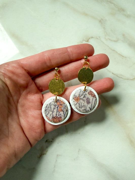 Hand holding a pair of earrings with floral designs on a marble surface