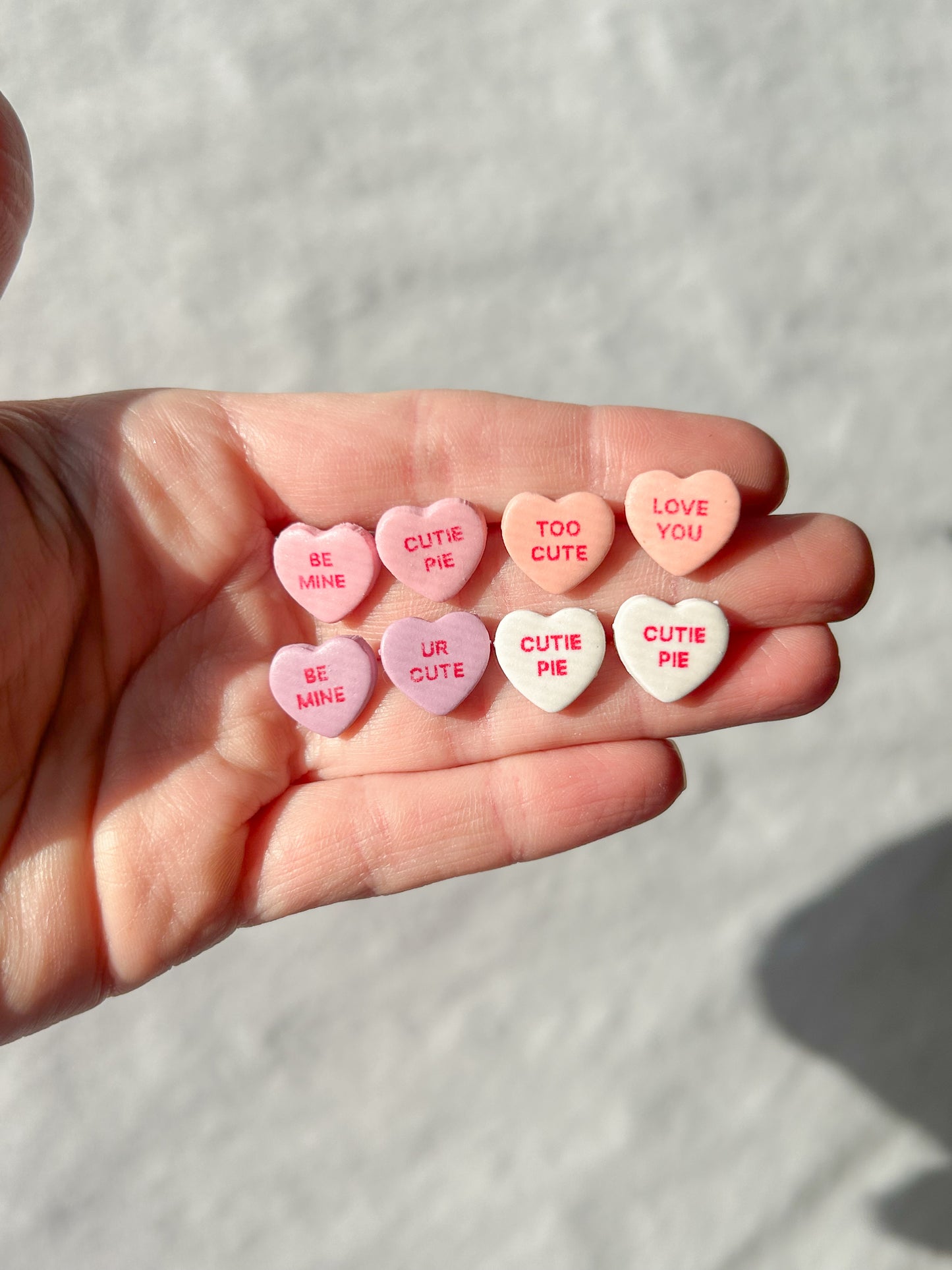 Hand holding small candy hearts with various messages on a light background