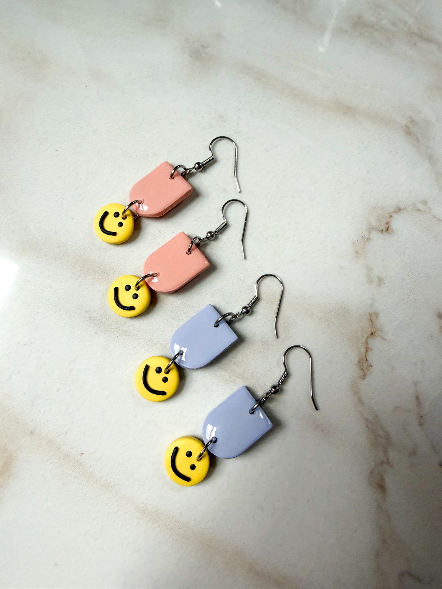 Pair of earrings with smiley face charms on a marble surface